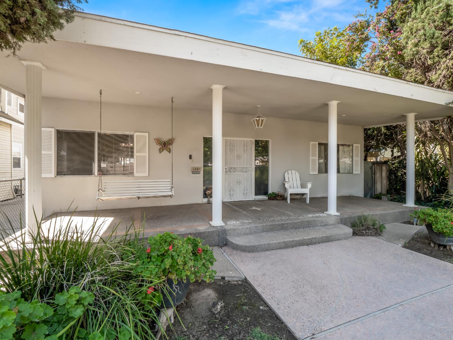 Single-story home with a broad covered porch, white columns, hanging swing, and planted entry.