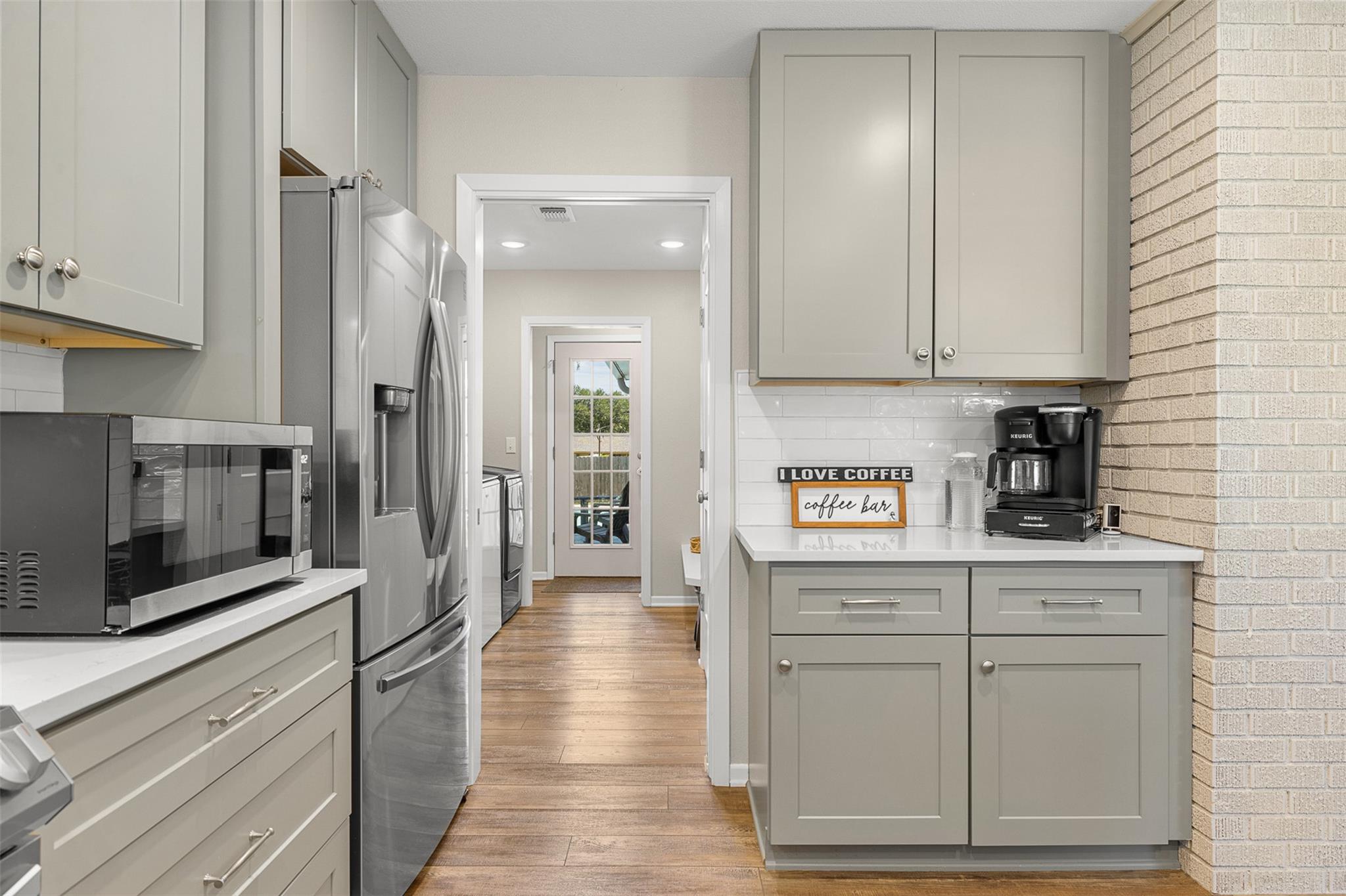 Kitchen with gray cabinets, stainless steel appliances, wood flooring, and a coffee bar.