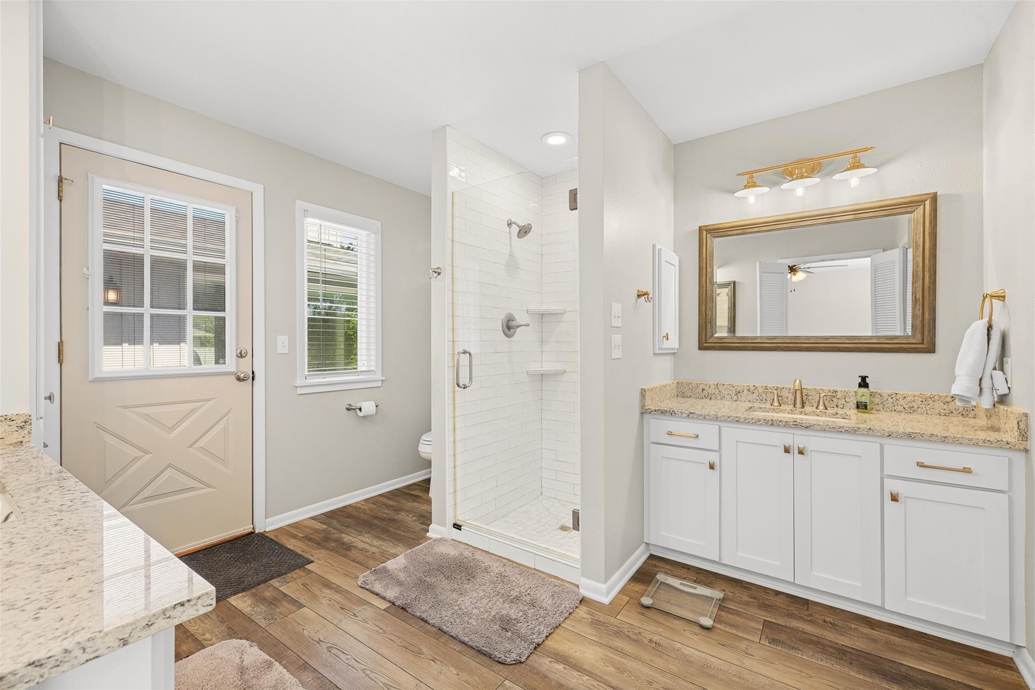 Bathroom with a white tiled walk-in shower and granite vanity beside a windowed exterior door.