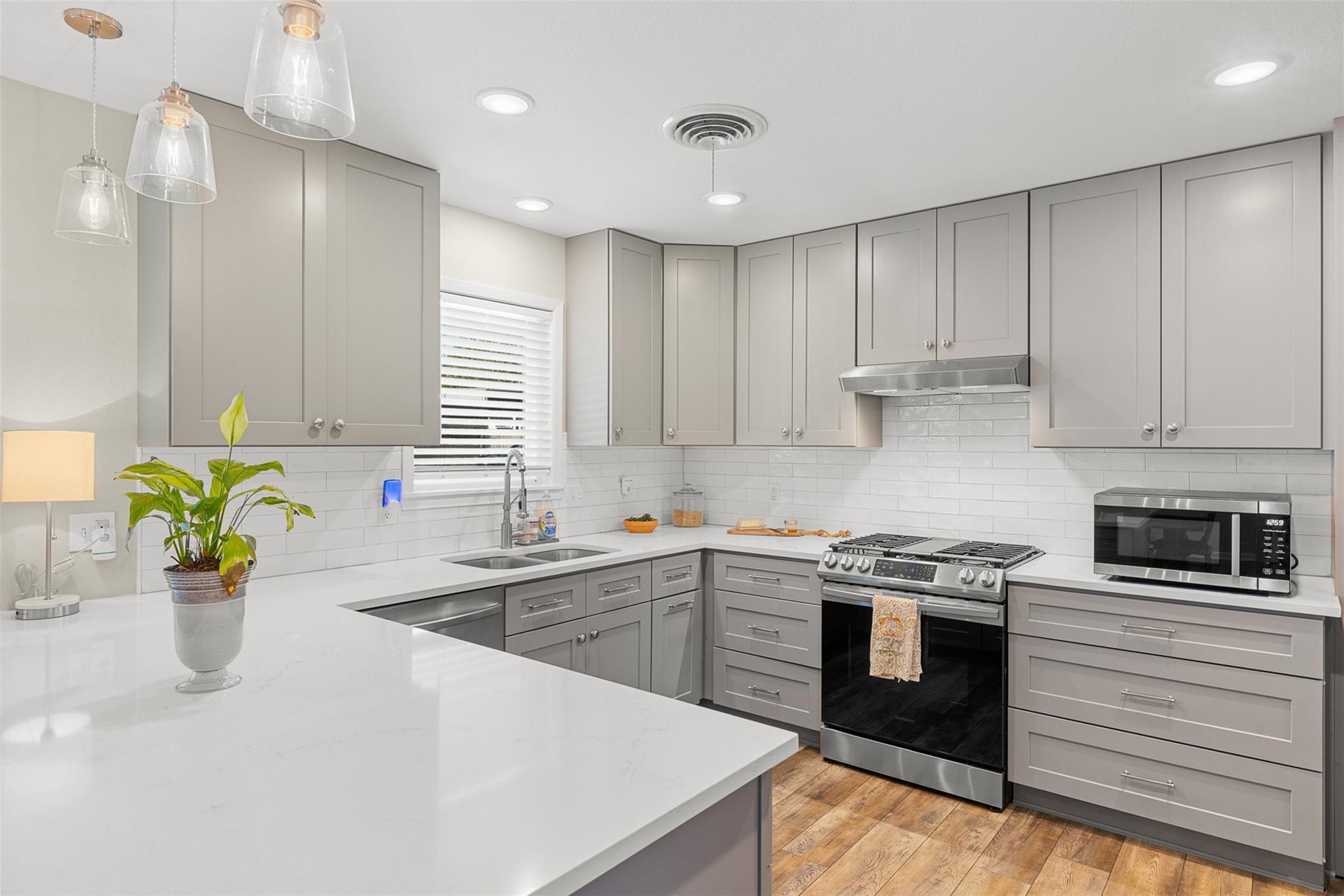 Kitchen with gray cabinetry, white counters, stainless steel range, and a large peninsula.