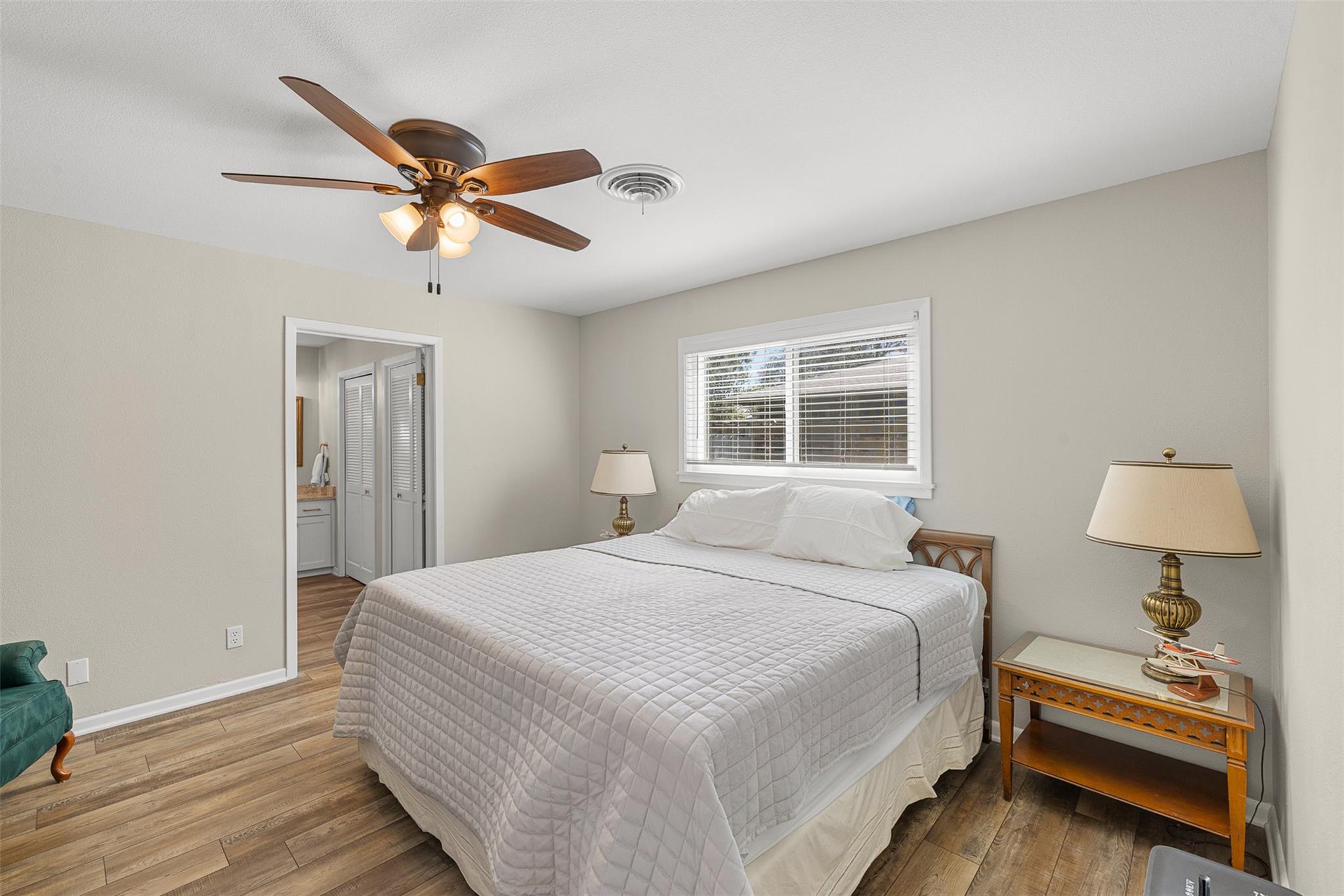 Bedroom with a wood-floor, ceiling fan, and doorway to an adjoining bathroom.