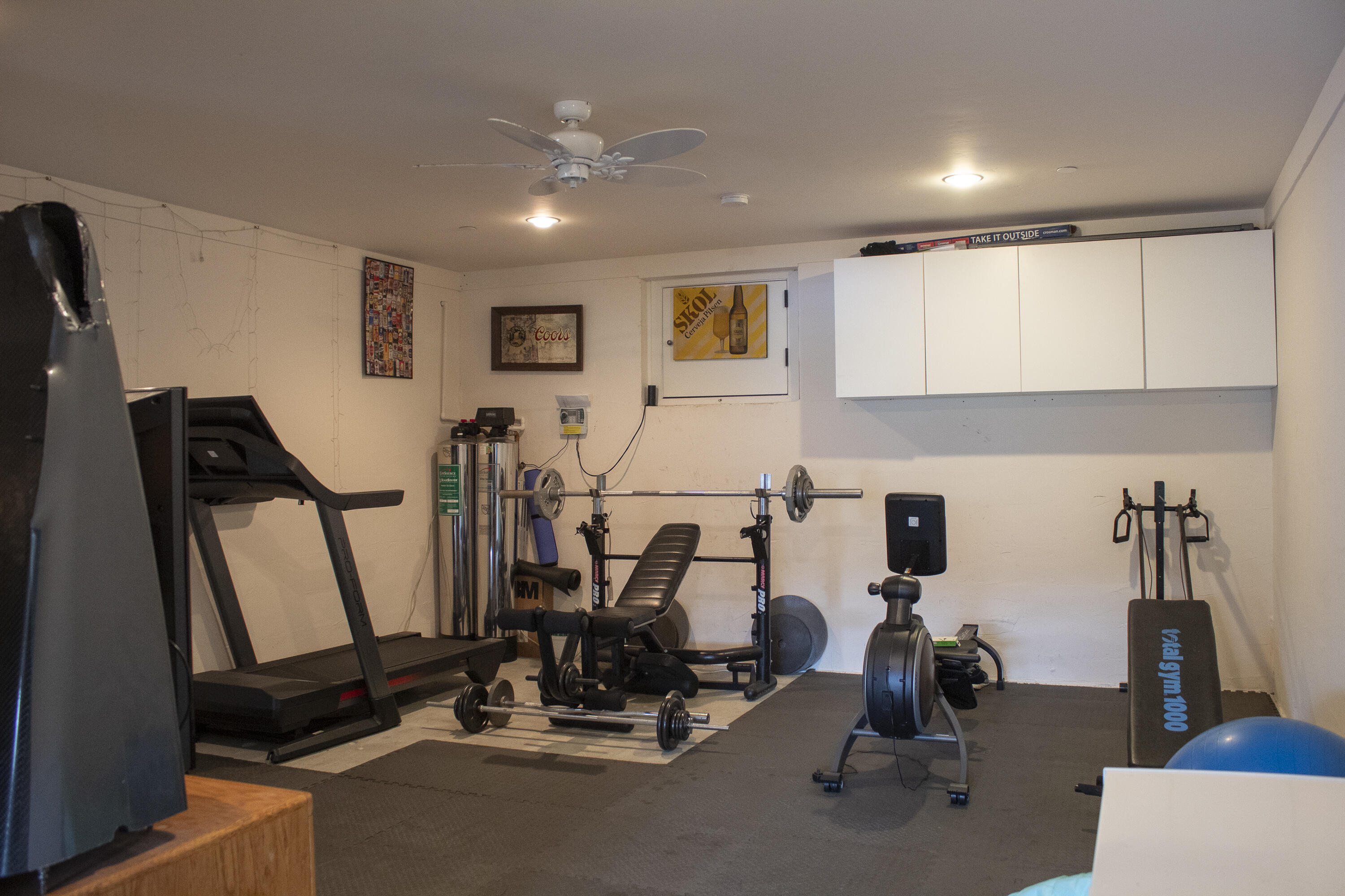 Home gym with a treadmill, weight bench and barbell, exercise bike, and strength-training equipment.