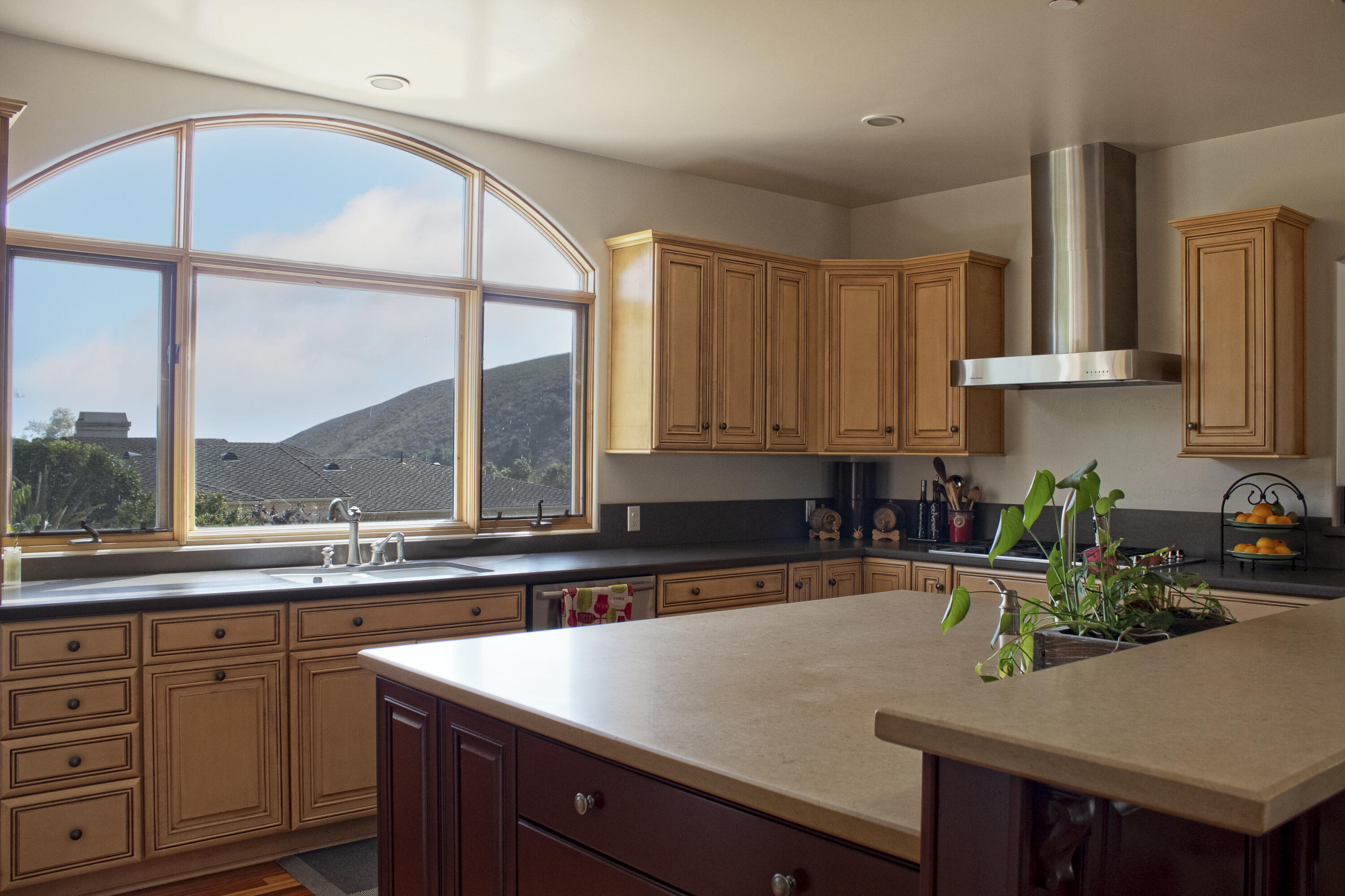 Kitchen with warm wood cabinets, a large island, and an arched window overlooking a hillside.