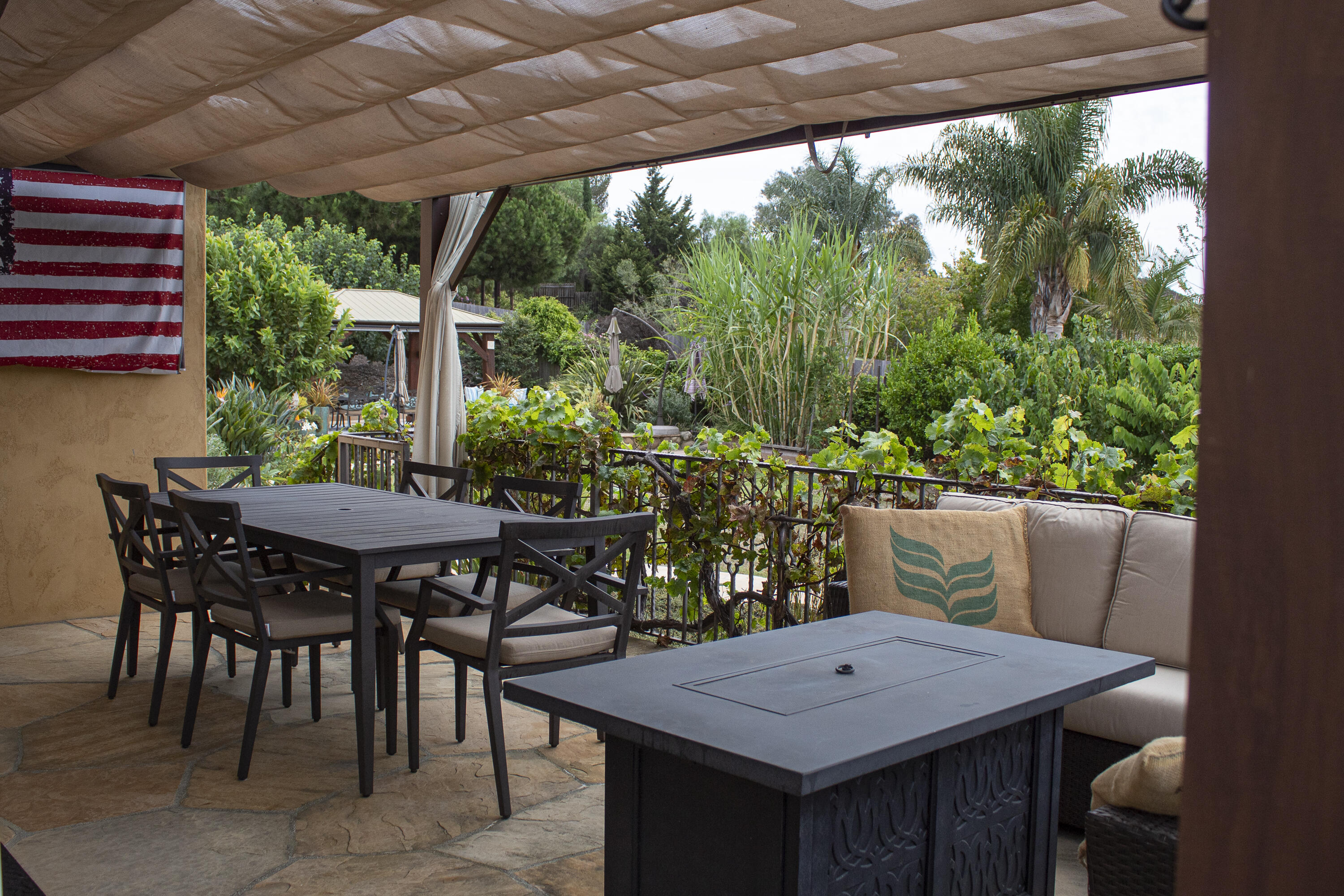Covered patio with dining furniture, lounge seating, a fire table, and lush garden views.