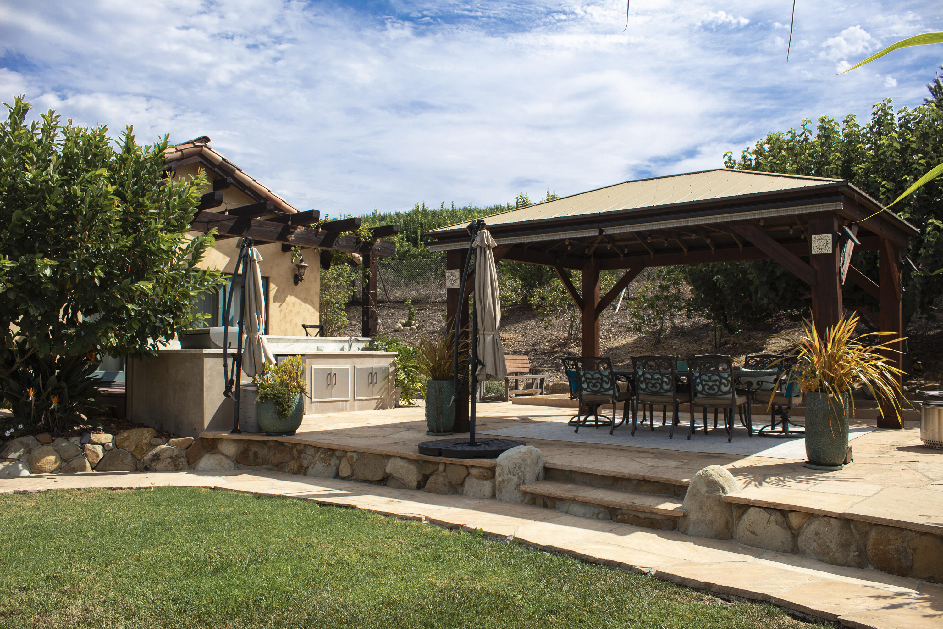 Backyard patio with an outdoor kitchen and a covered pavilion over a dining table.