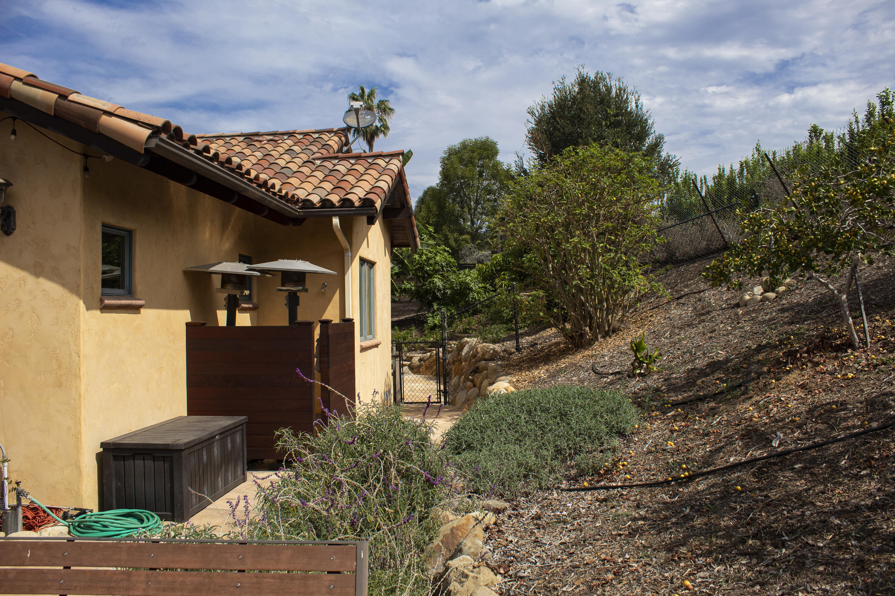 Stucco home with a terracotta tile roof beside a small patio and landscaped hillside.