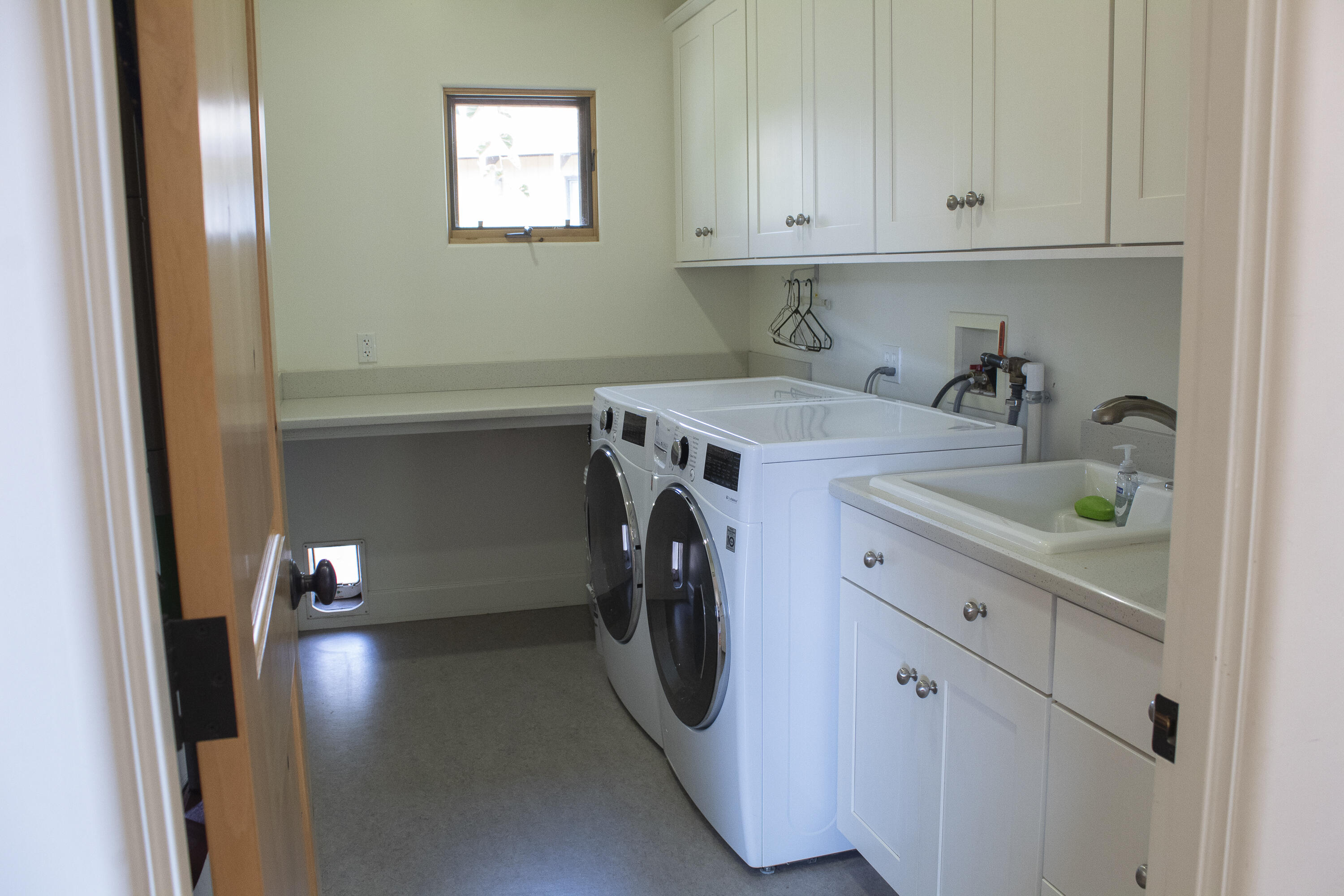 Laundry room with front-loading washer and dryer, white cabinets, folding counter, and utility sink.