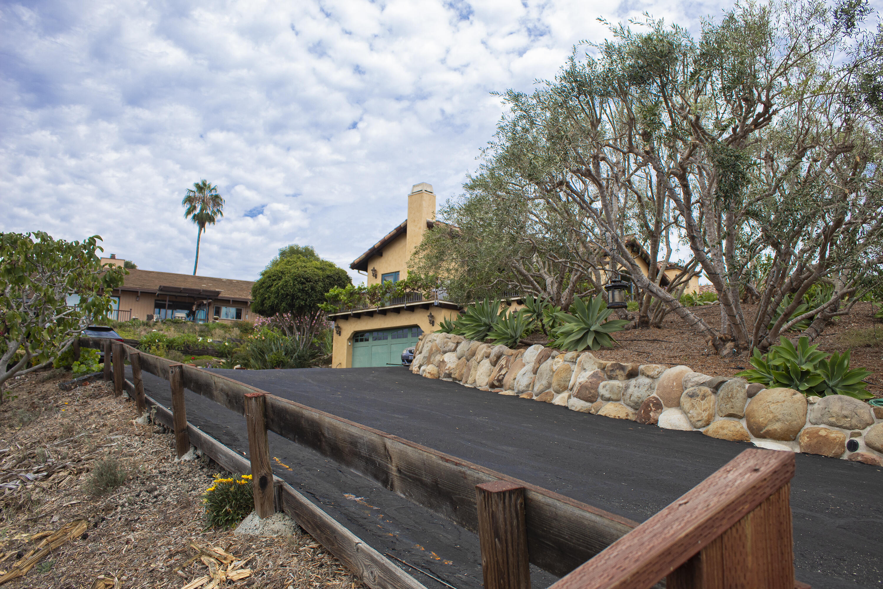 Tan stucco home with green garage door, stone retaining wall, and landscaped driveway.