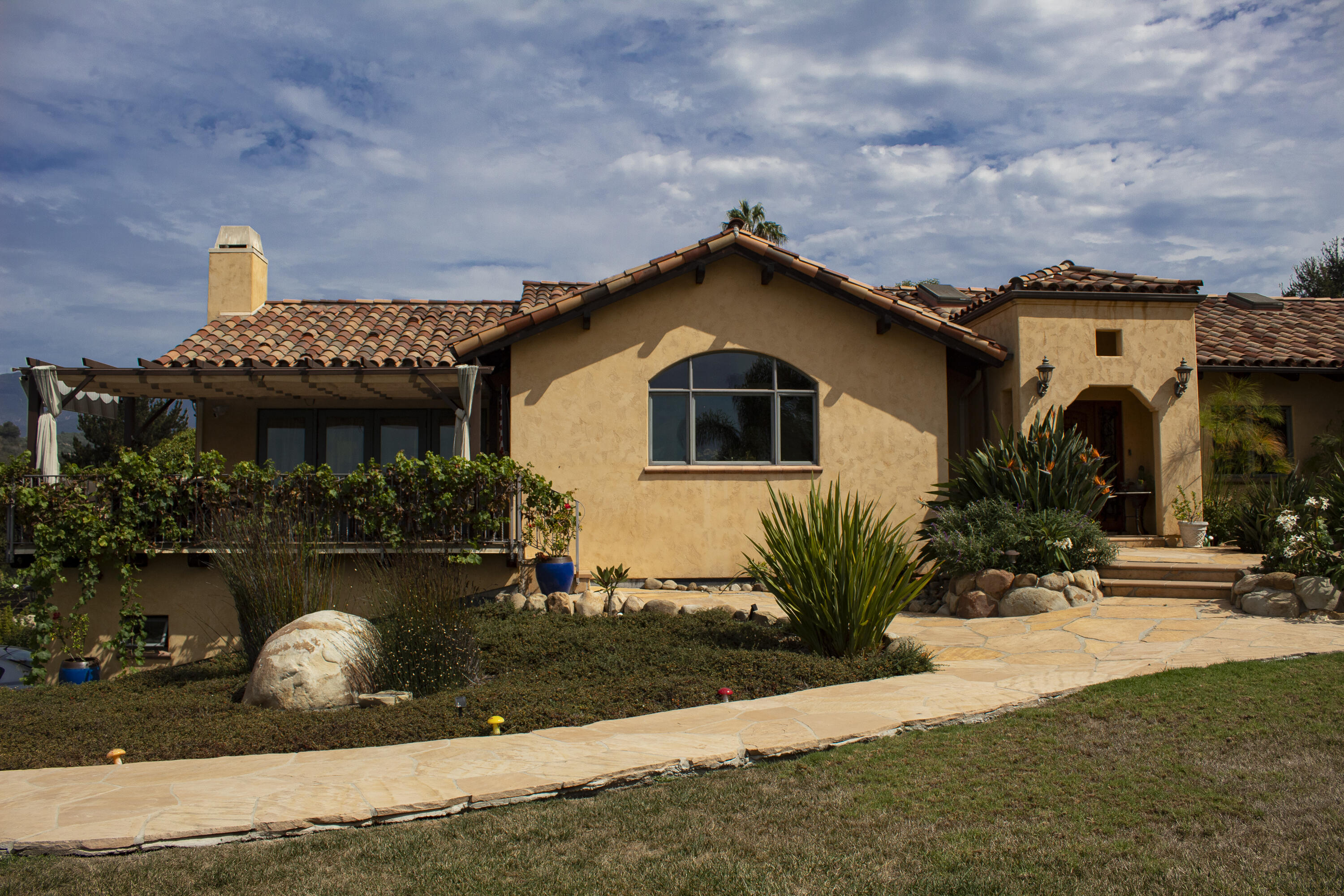 Tan stucco home with a red tile roof, covered patio, and landscaped stone walkway.