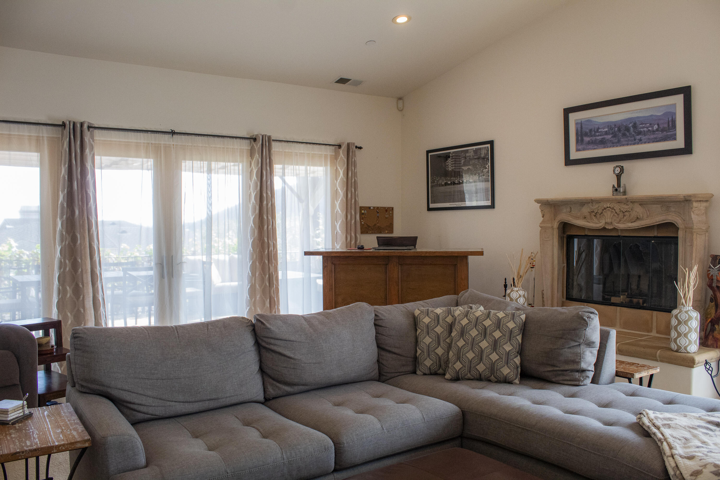 Living room with a gray sectional sofa, ornate stone fireplace, and wide glass doors to a deck.