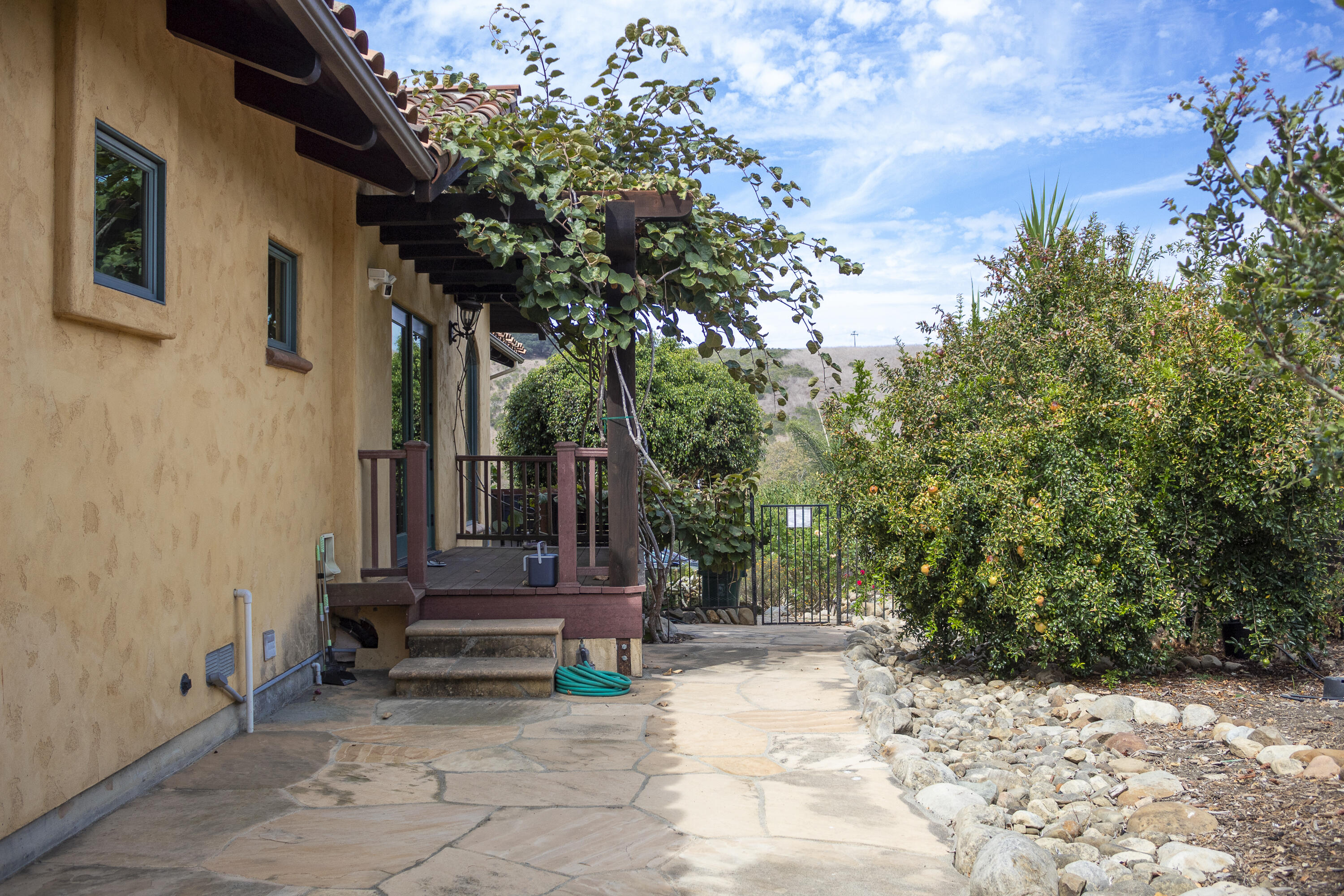 Stucco home and wooden porch beside a stone walkway, citrus trees, and a rock garden.