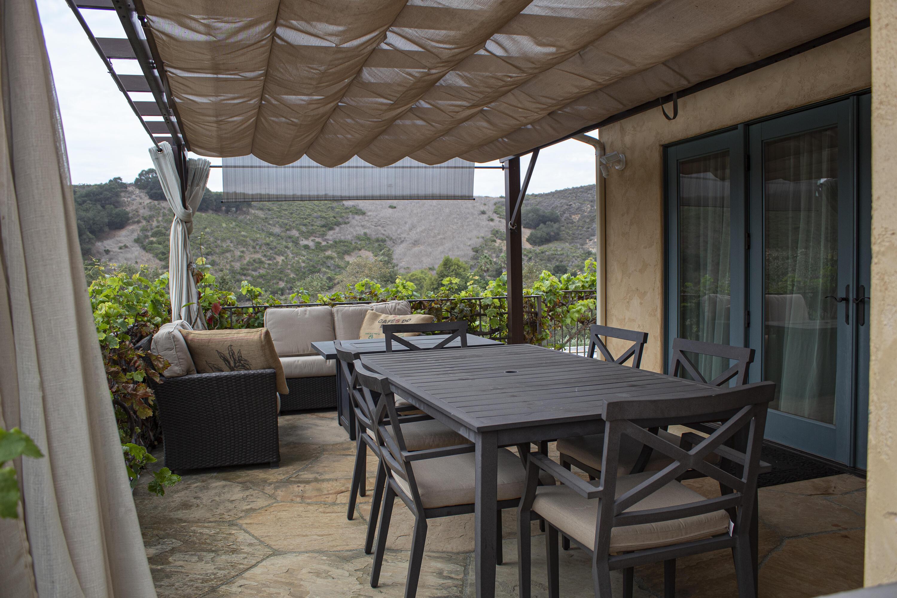 Stone patio with pergola, outdoor dining set, lounge seating, and views of rolling hills.
