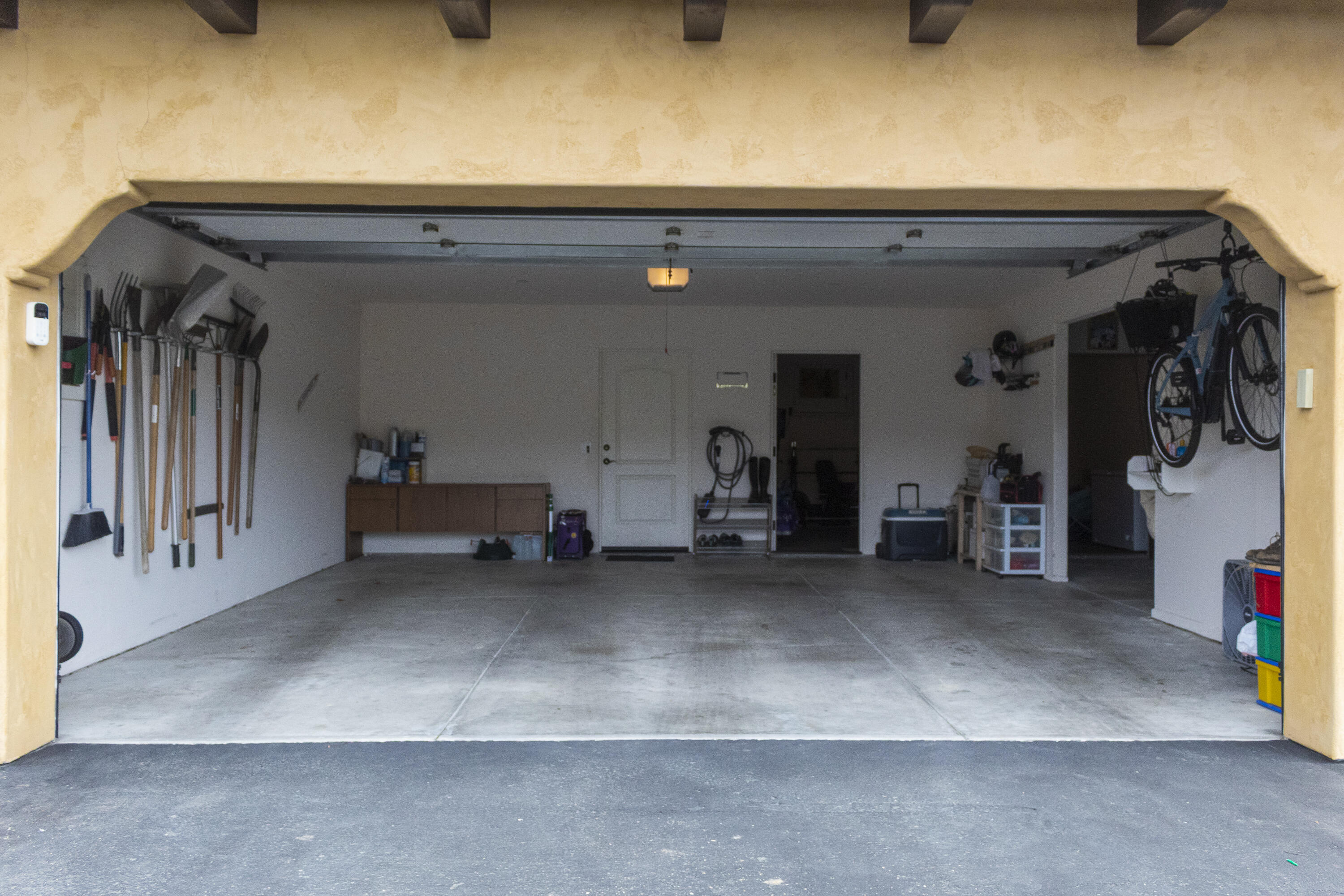 Open two-car garage with a mostly clear concrete floor, garden tools, and bicycles.