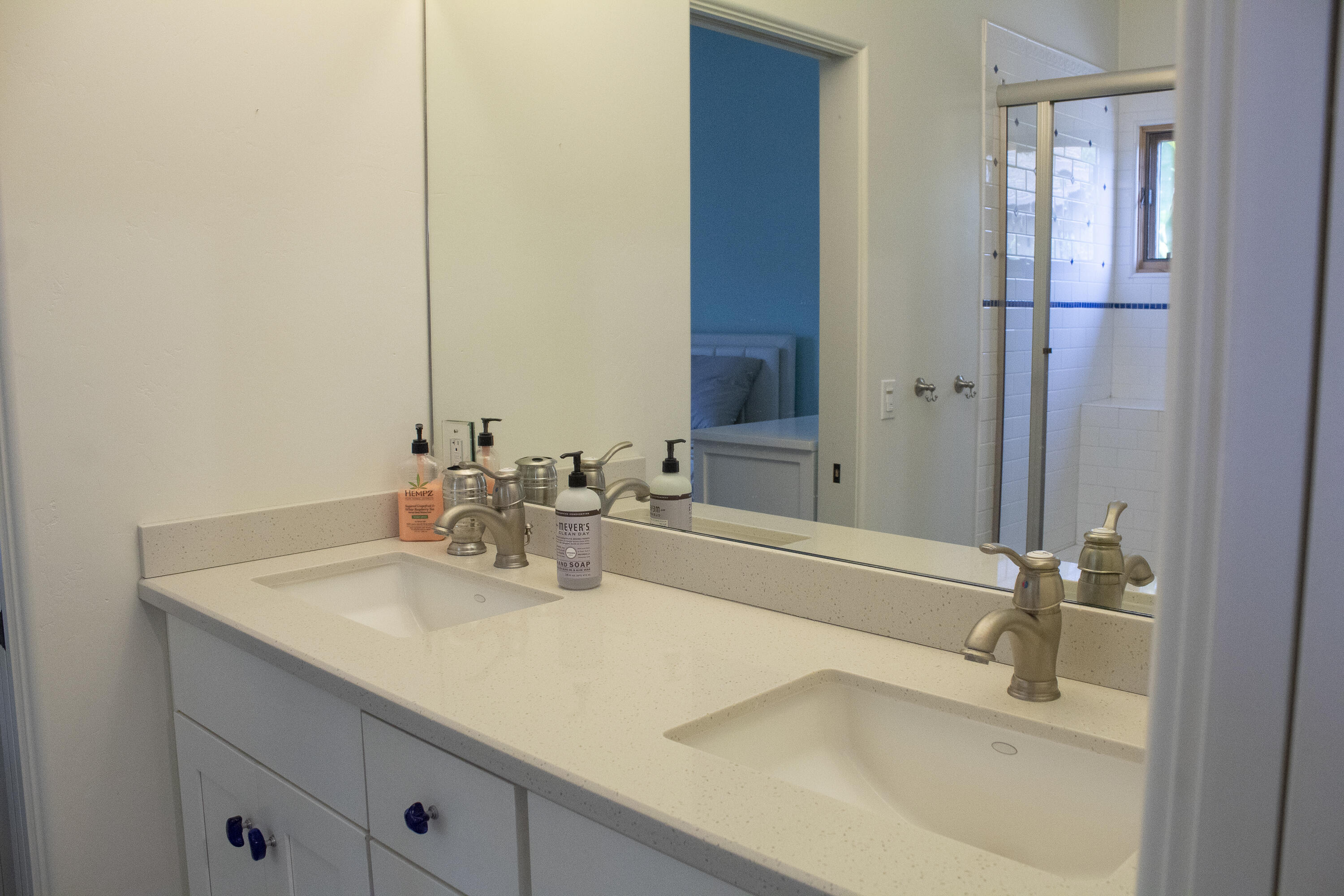 Bathroom double vanity with a large mirror reflecting a tiled glass-enclosed shower.