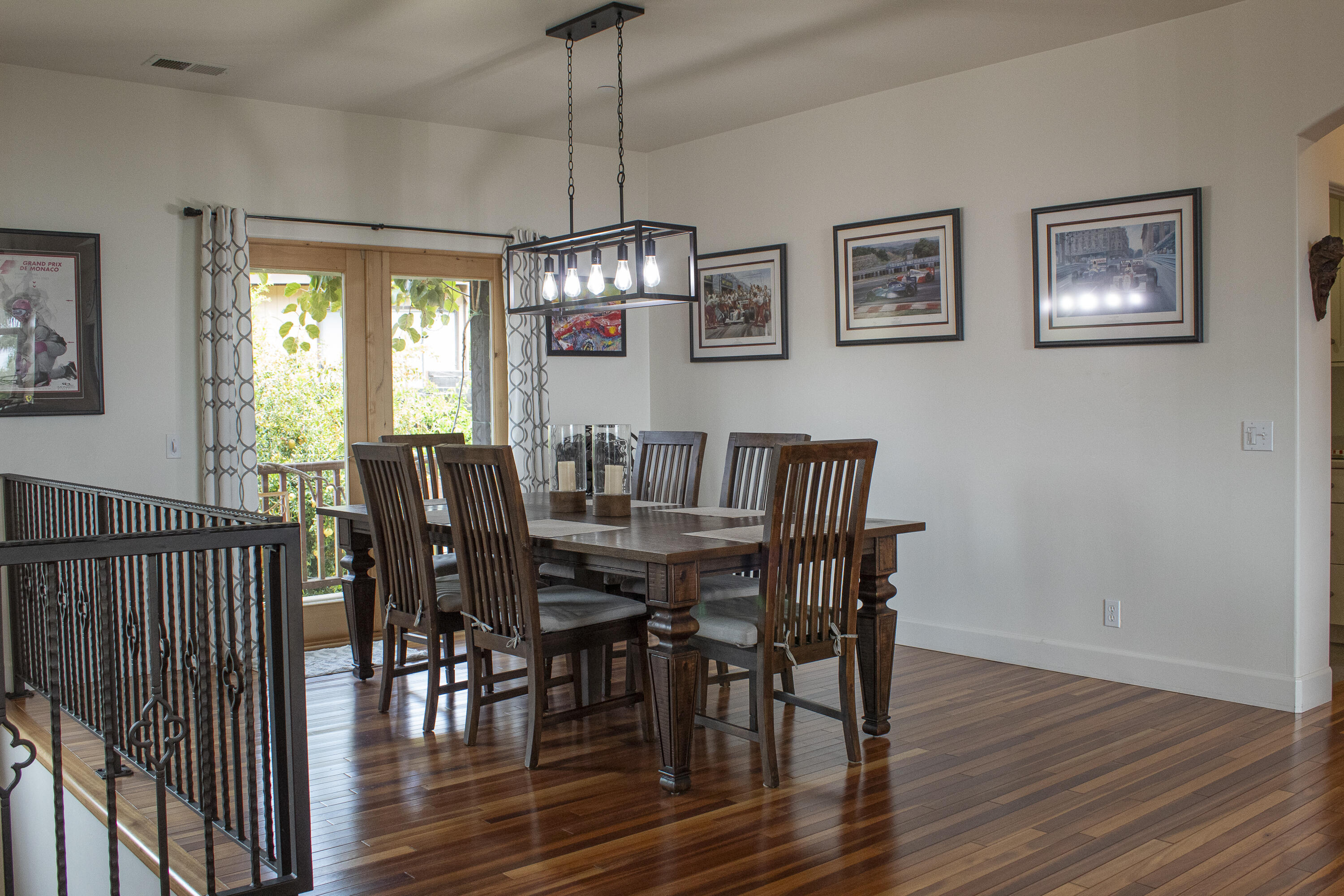 Dining room with a dark wood table, framed racing art, and glass doors opening to greenery.