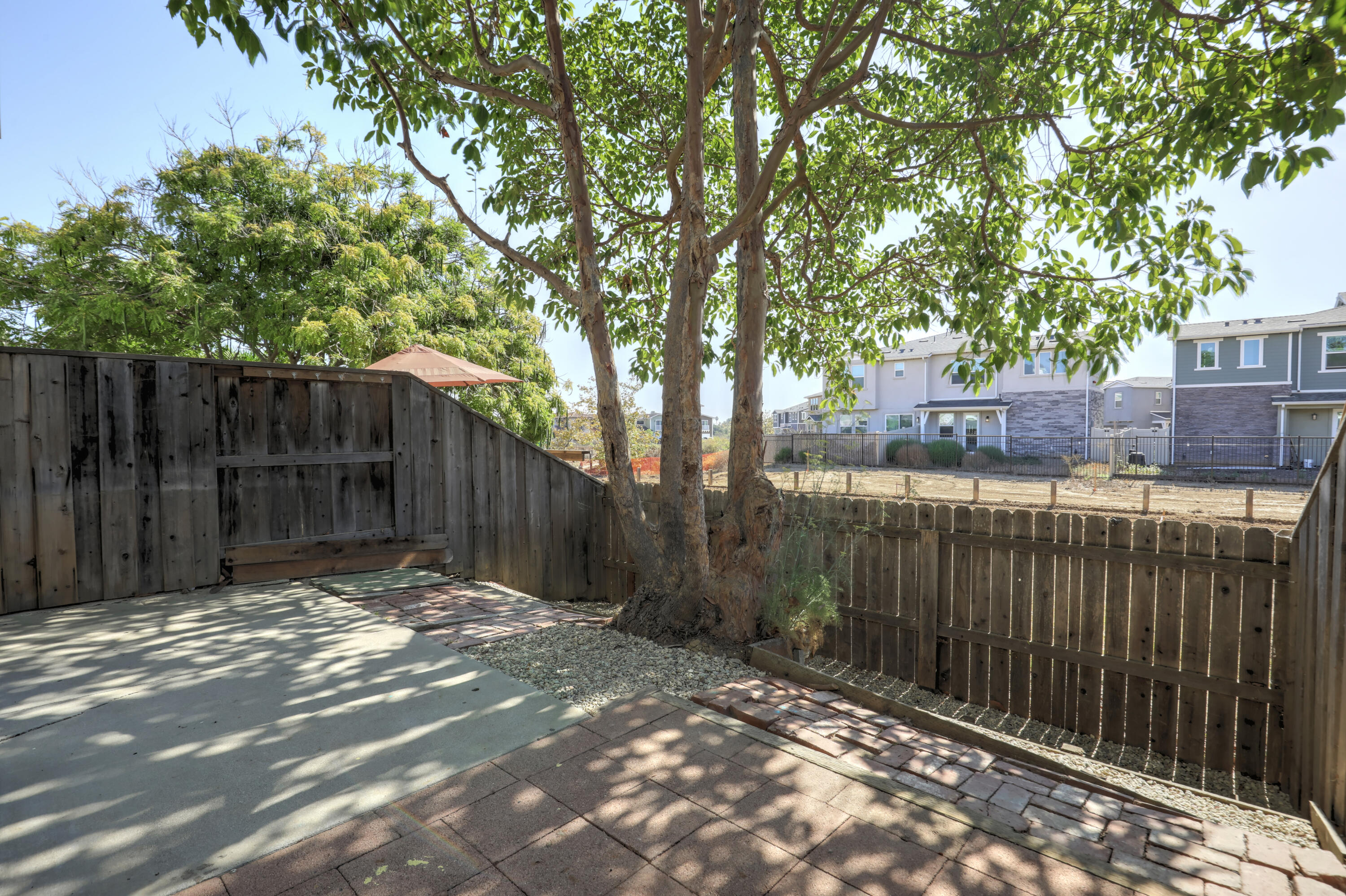Fenced patio with brick and concrete paving, a large shade tree, and a built-in bench.