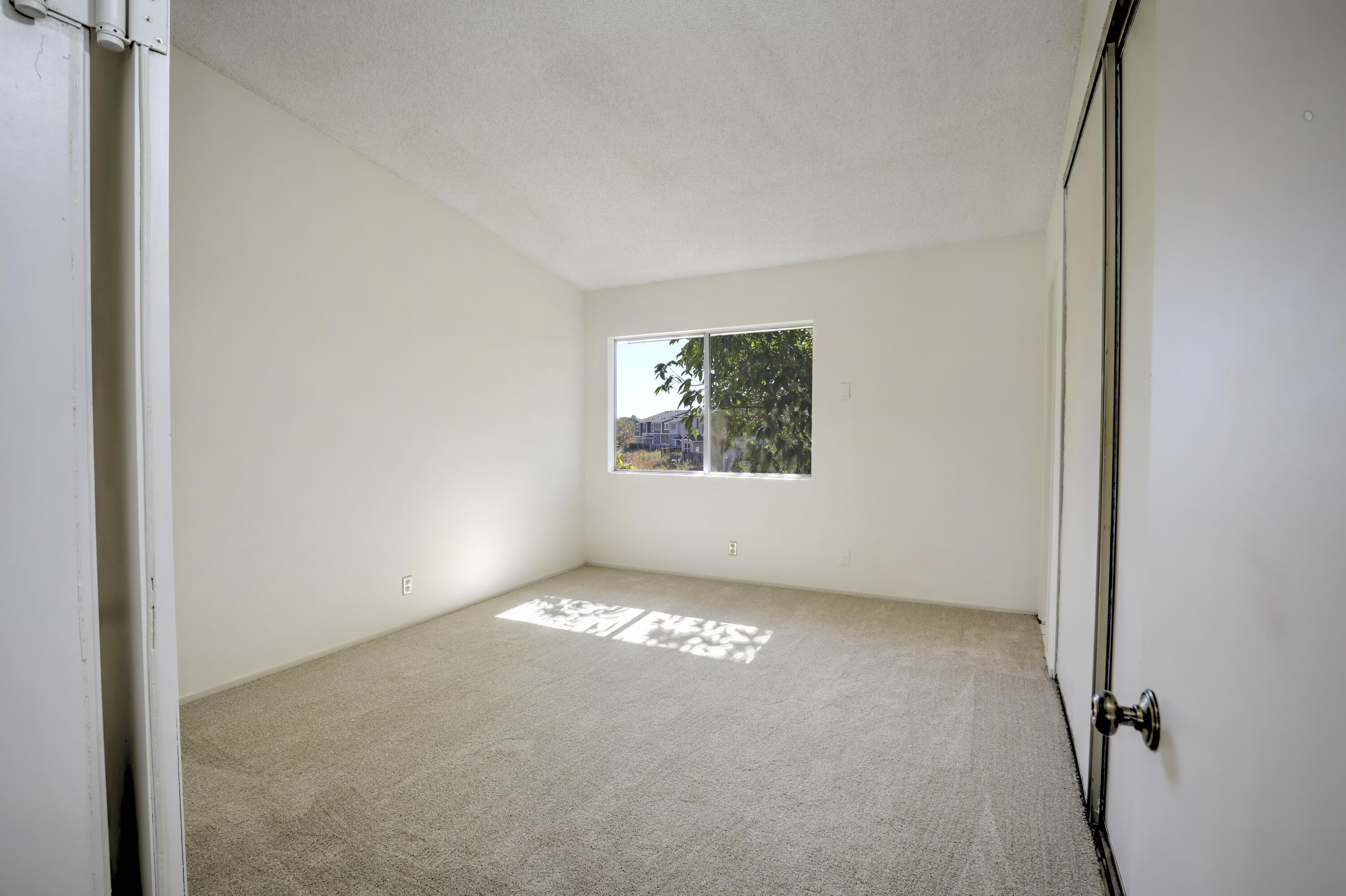 Empty carpeted bedroom with a window and sliding closet doors.