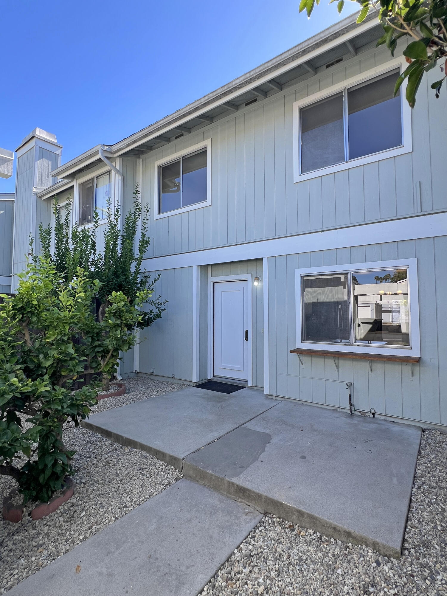 Light blue-gray two-story home with a concrete entry path and leafy shrubs.