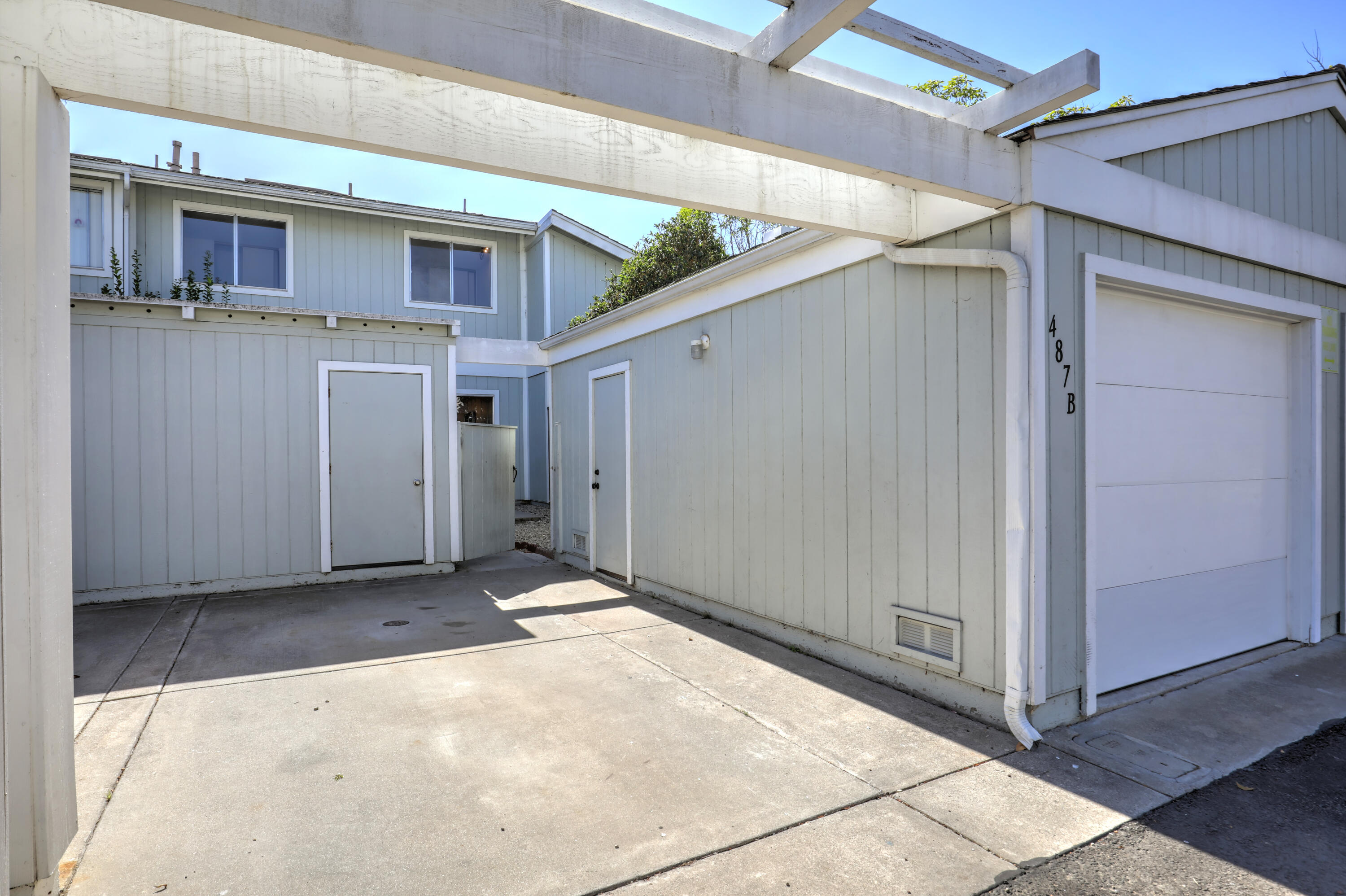 Residence courtyard and driveway beneath a white pergola, beside a garage marked 487 B.