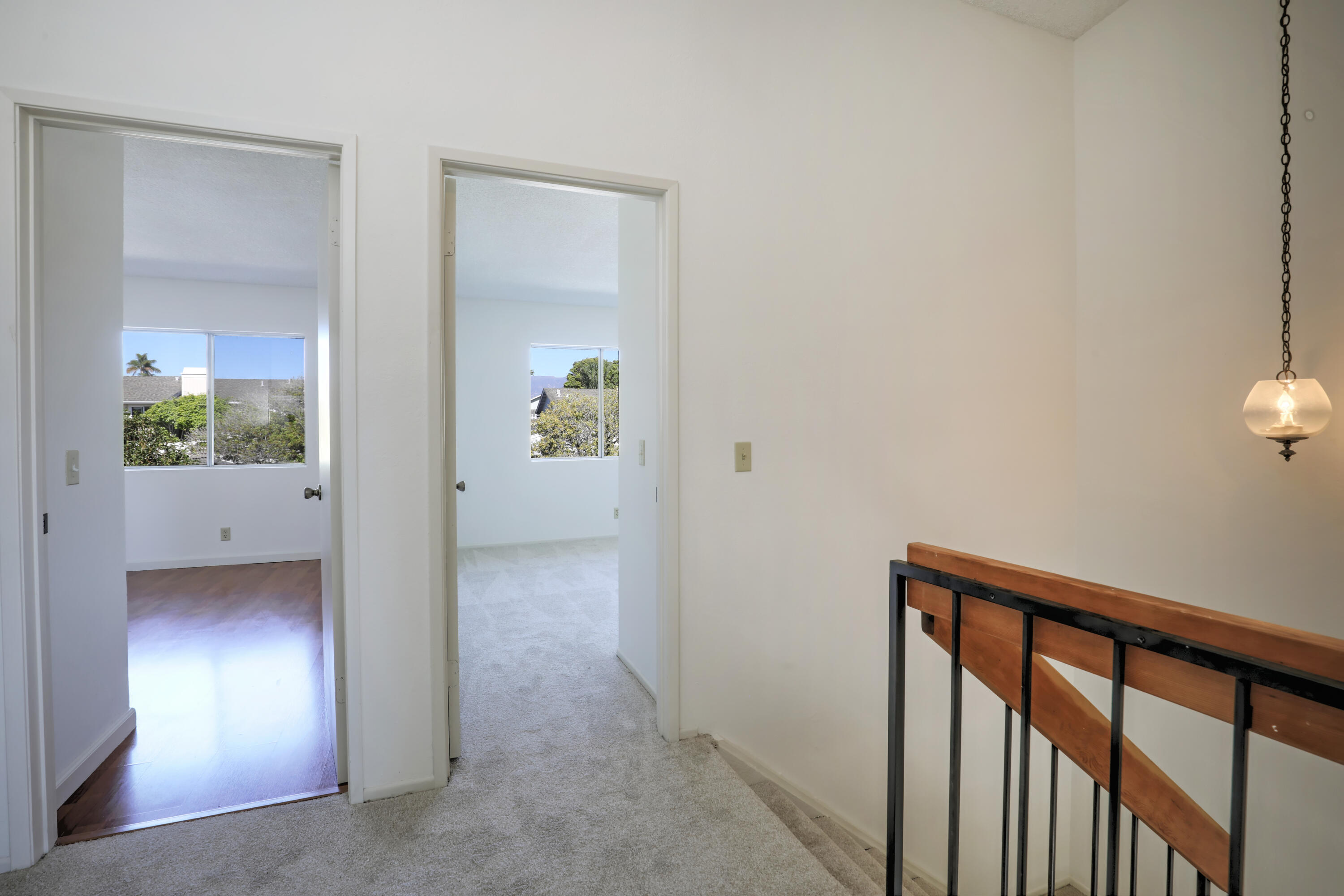 Carpeted upstairs landing with a stair railing and two open doorways to bright, empty rooms.