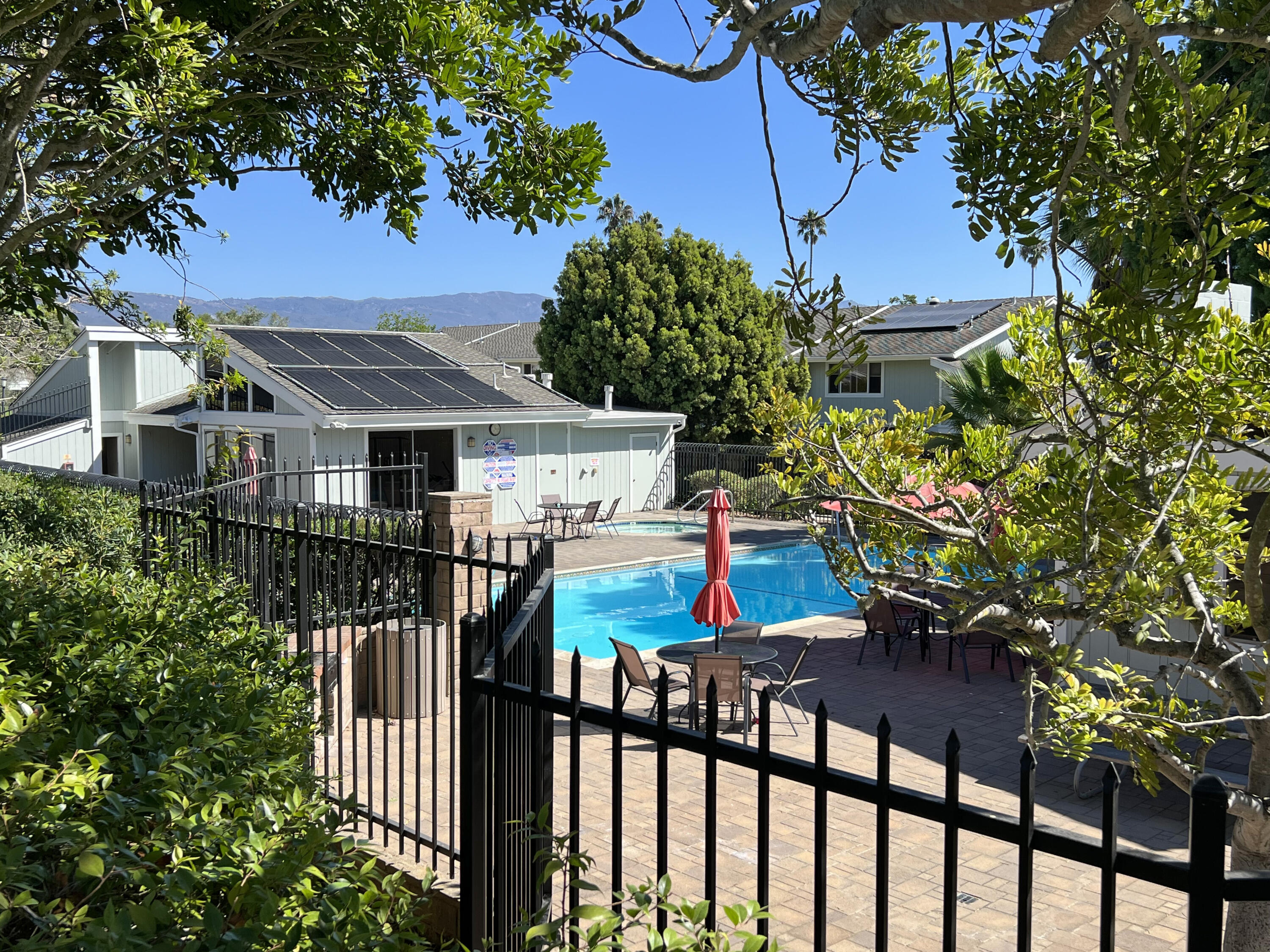 Community swimming pool and patio with red umbrellas, solar-paneled homes, and mountains beyond.