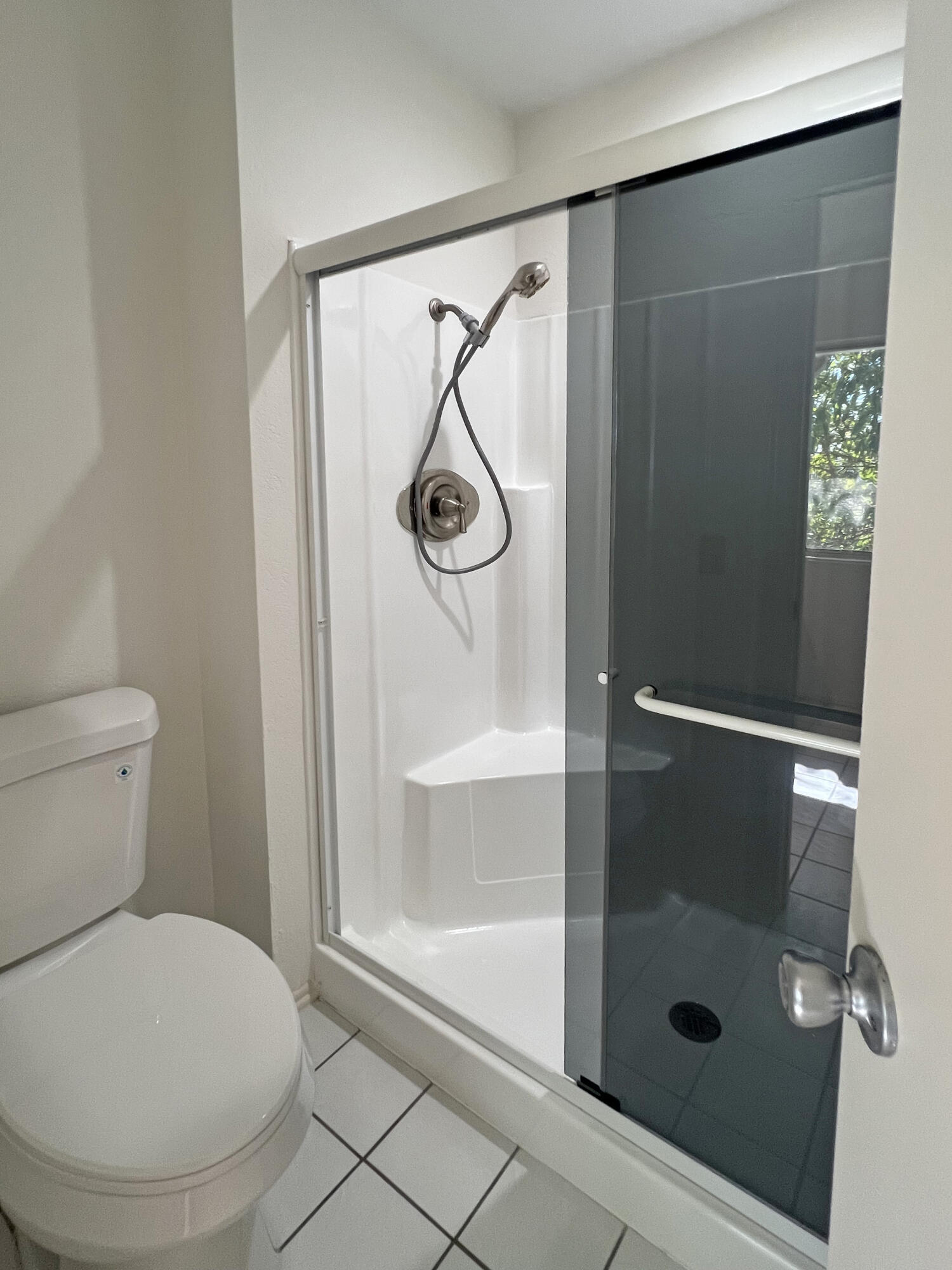 Bathroom with a white shower enclosure, sliding glass door, handheld showerhead, and toilet.