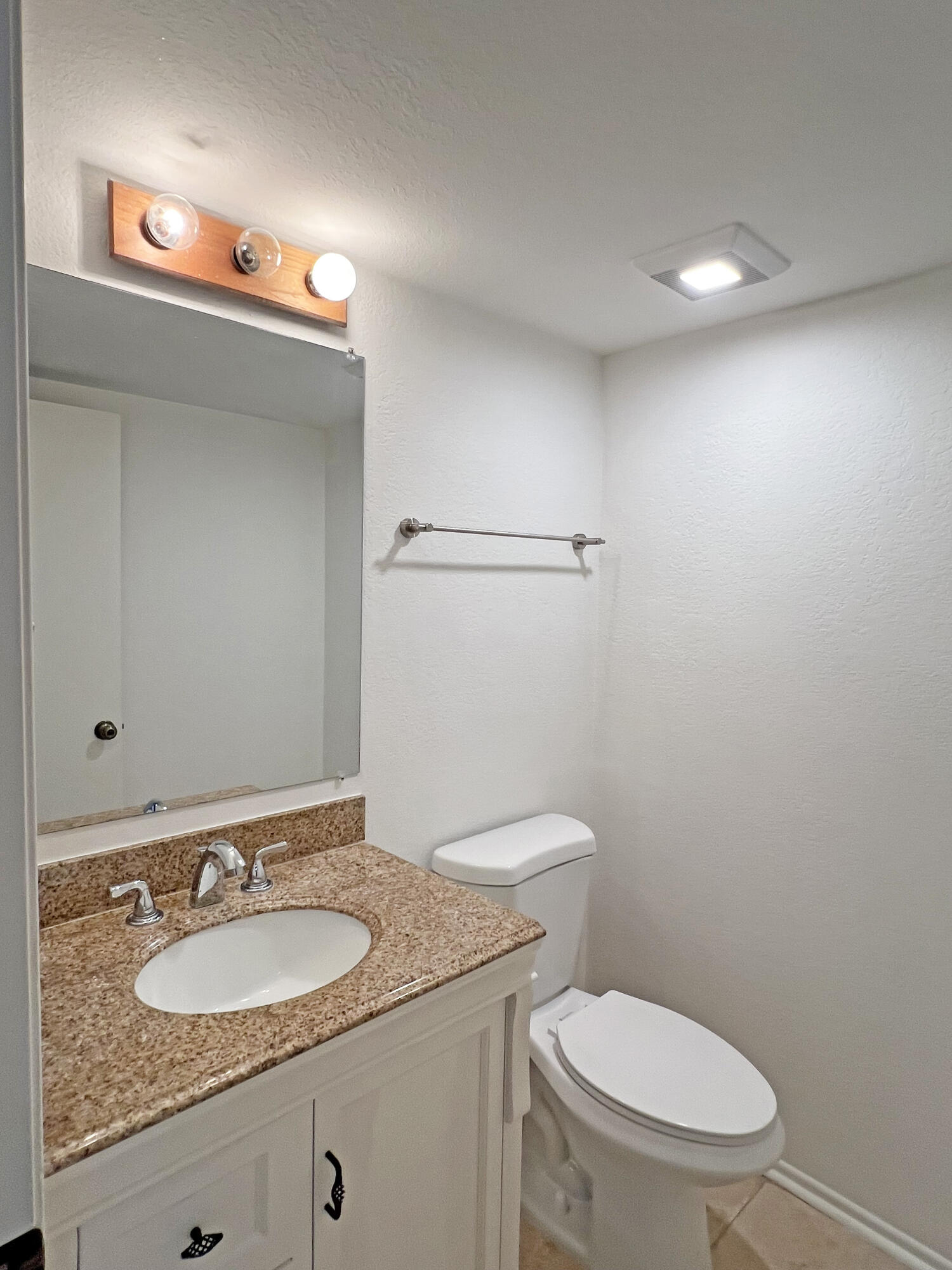 Bathroom with a speckled granite vanity, oval sink, large mirror, and toilet.