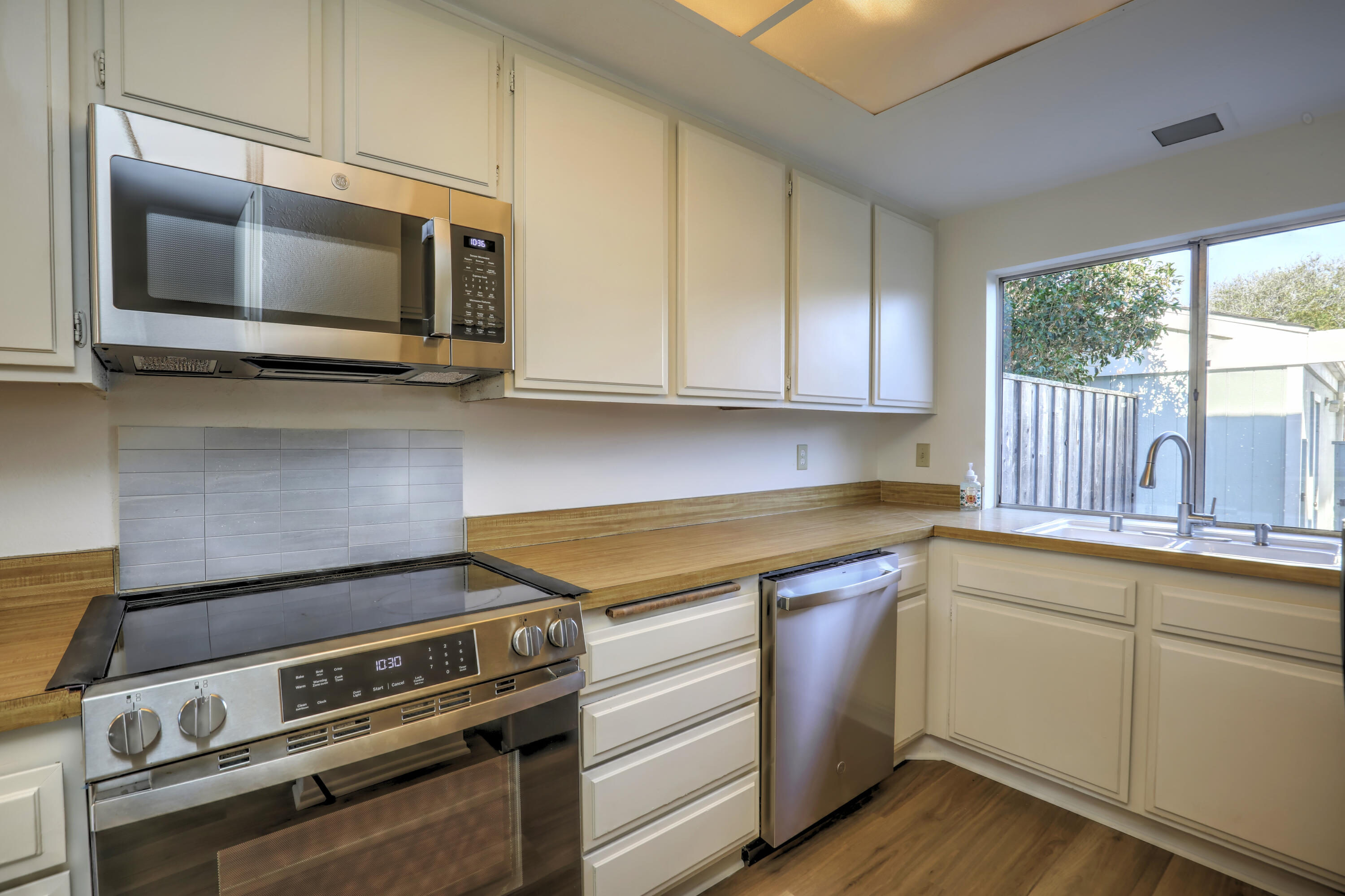 Kitchen with white cabinets, wood counters, stainless appliances, and a sink beneath a large window.