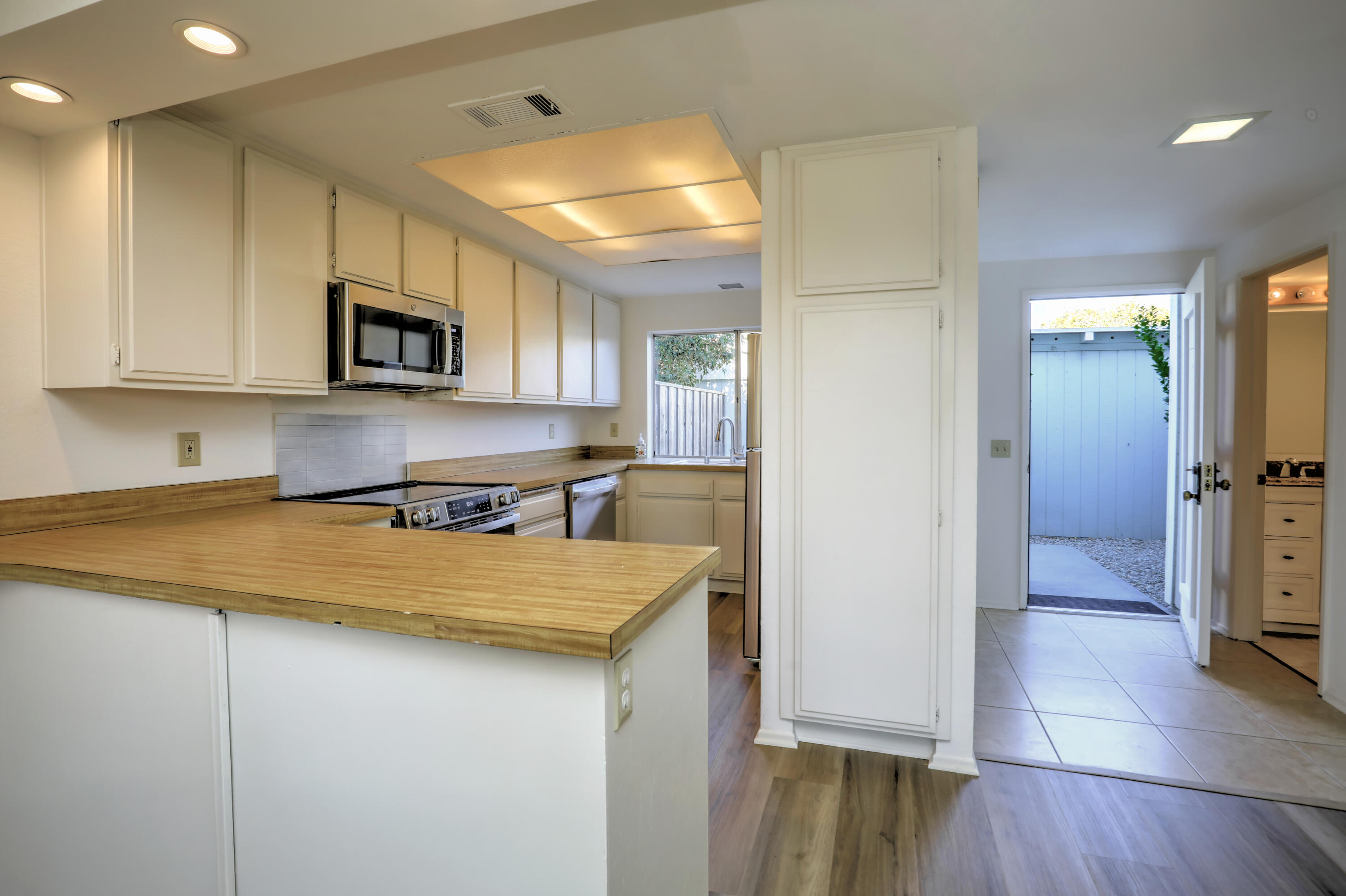 Kitchen with white cabinets, stainless-steel appliances, and a long wood countertop beside an open patio door.