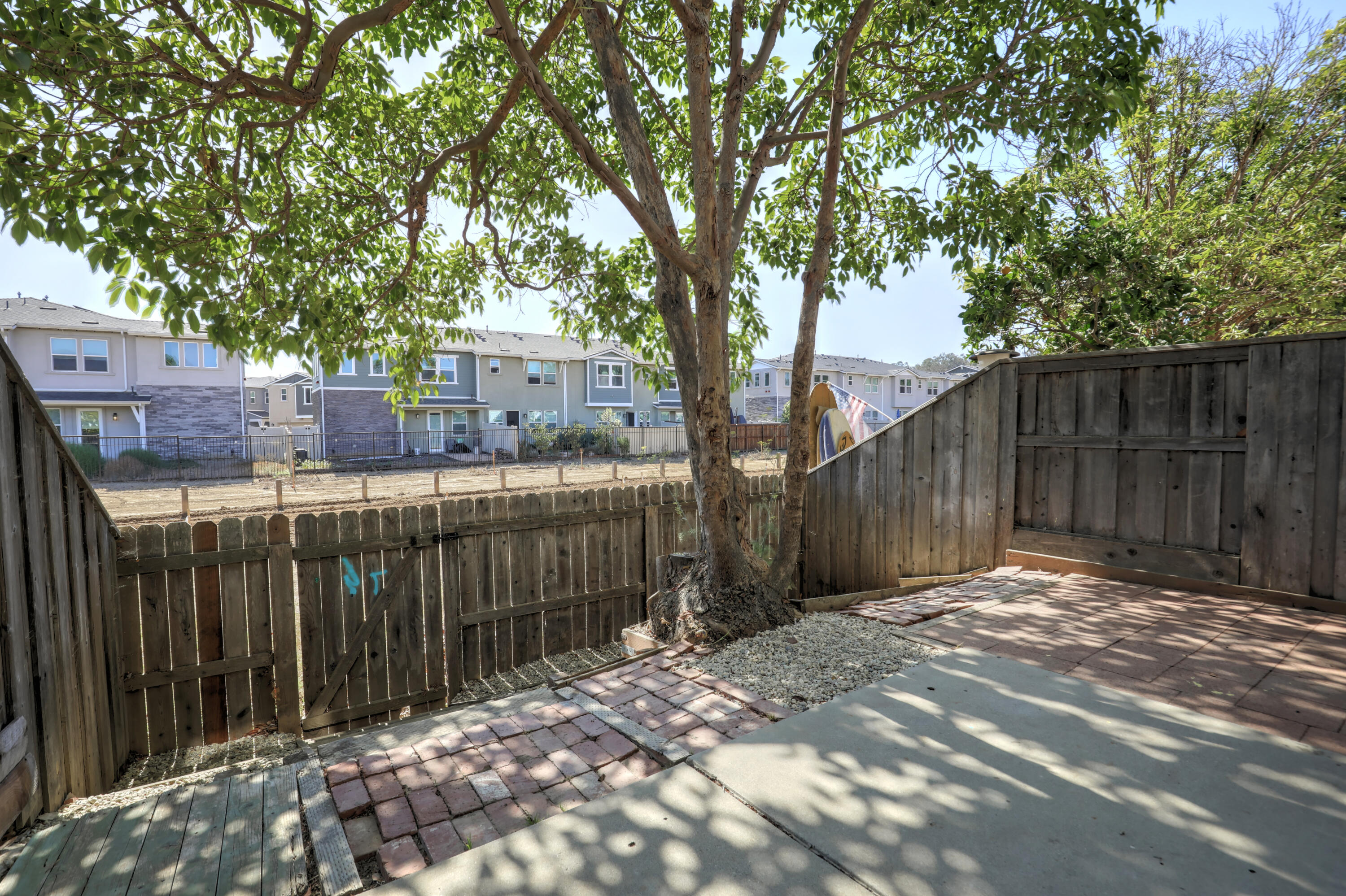 Fenced patio beneath a broad shade tree, with brick paving and neighboring townhomes beyond.