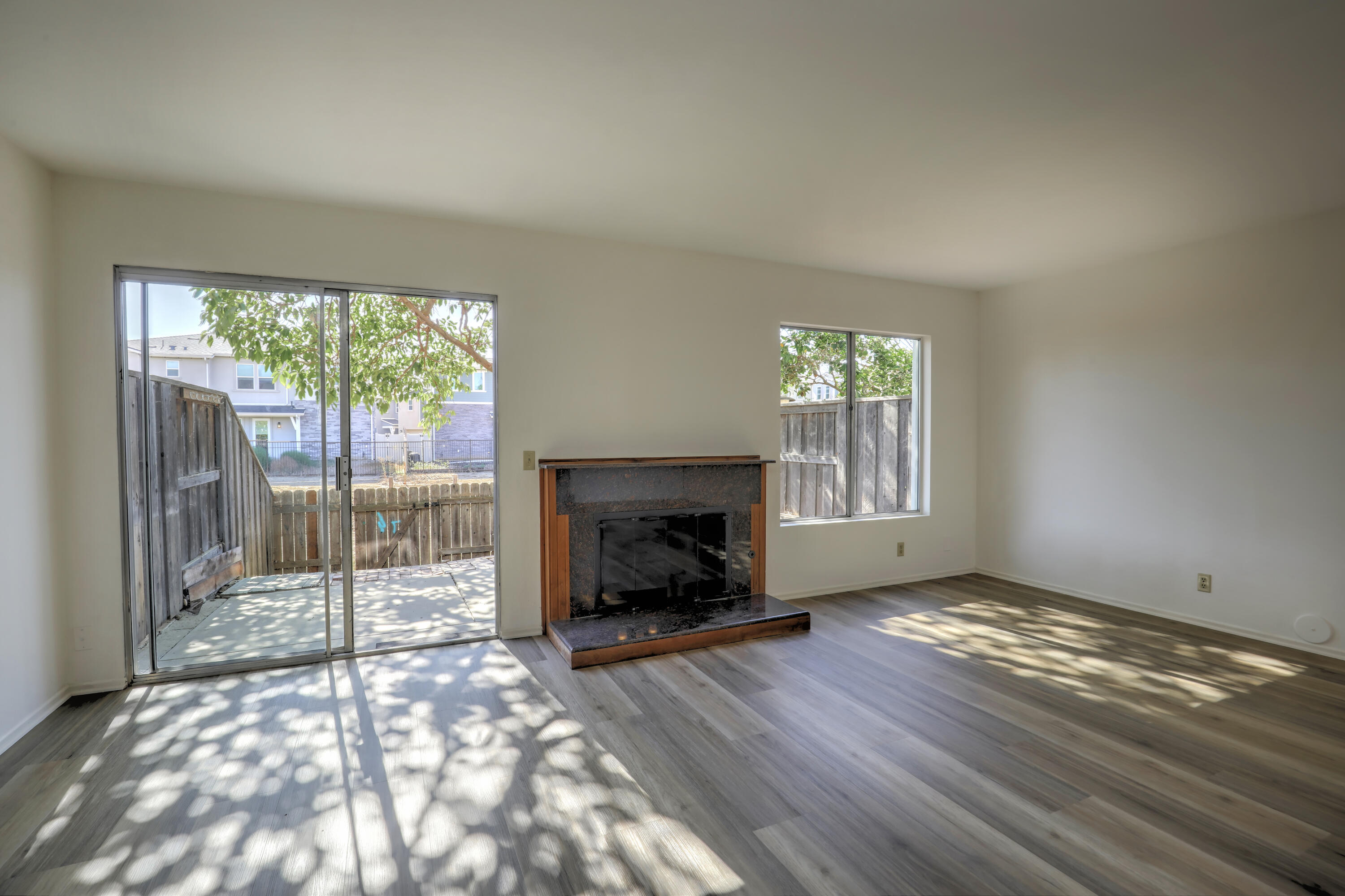 Empty living room with a dark stone fireplace and sliding glass door to a fenced patio.