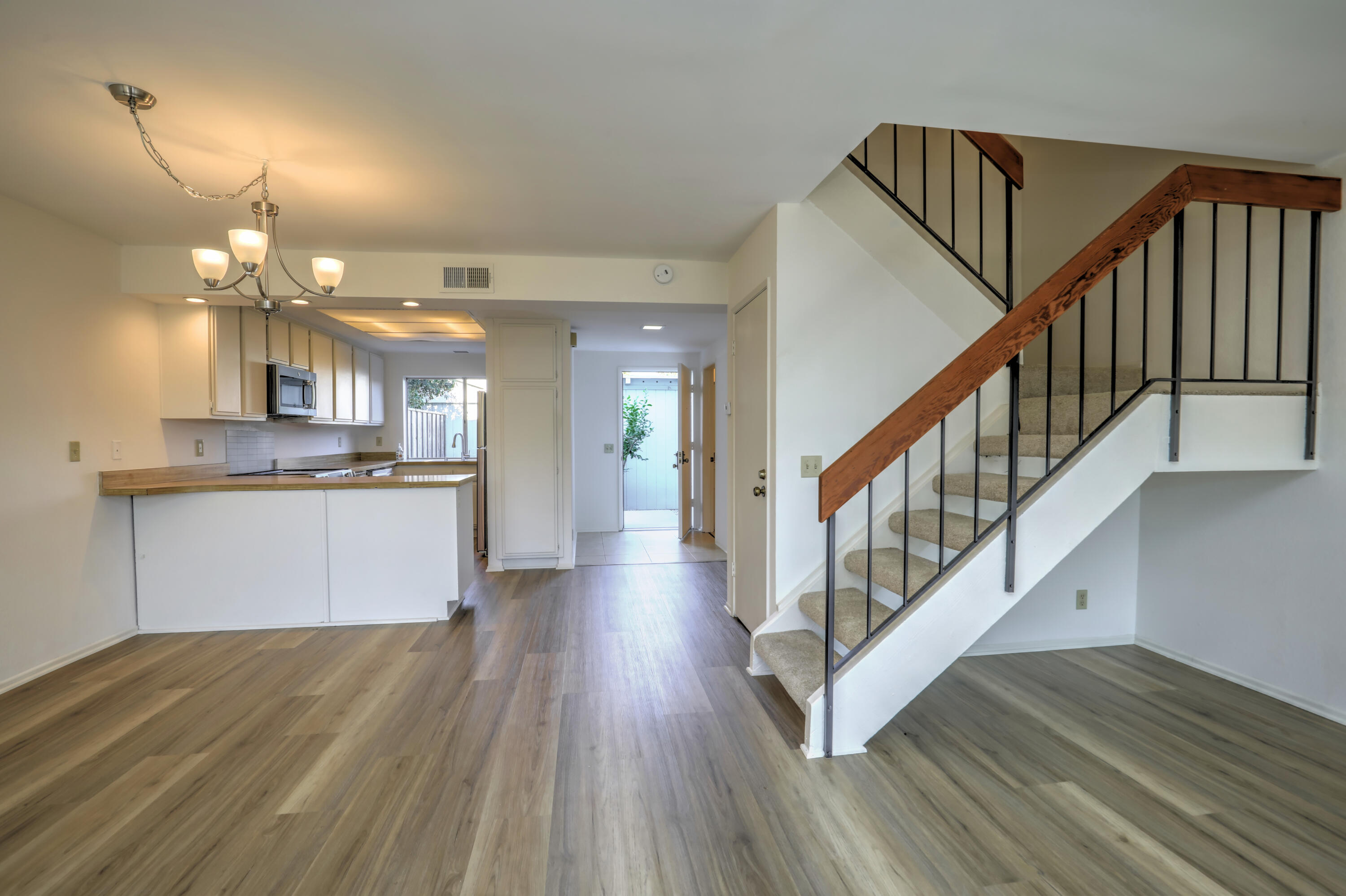 Open-plan kitchen and entry with wood-look floors and a carpeted staircase with a wooden handrail.