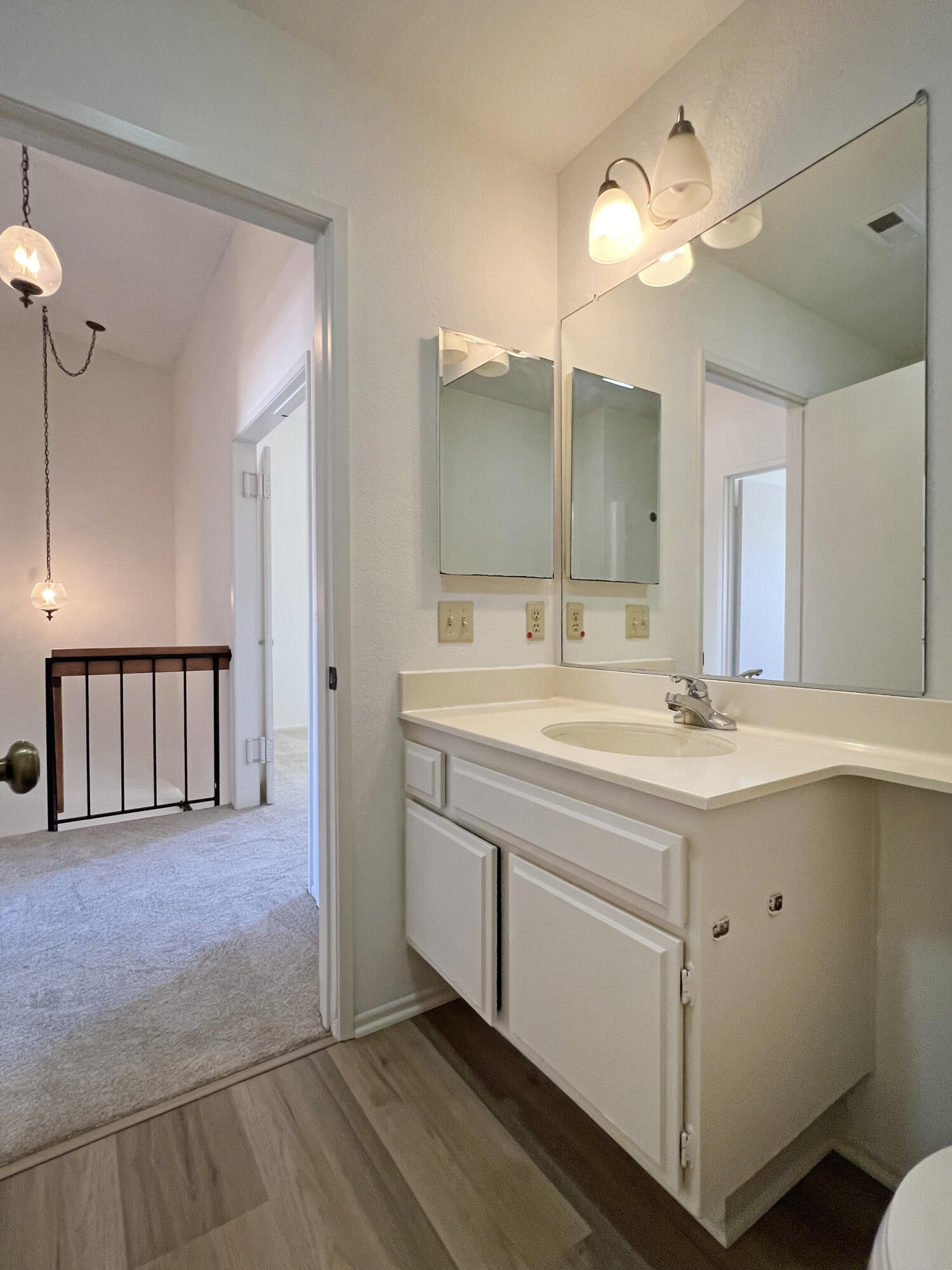Bathroom vanity with white cabinets, a single sink, large mirror, and lit vanity lights.