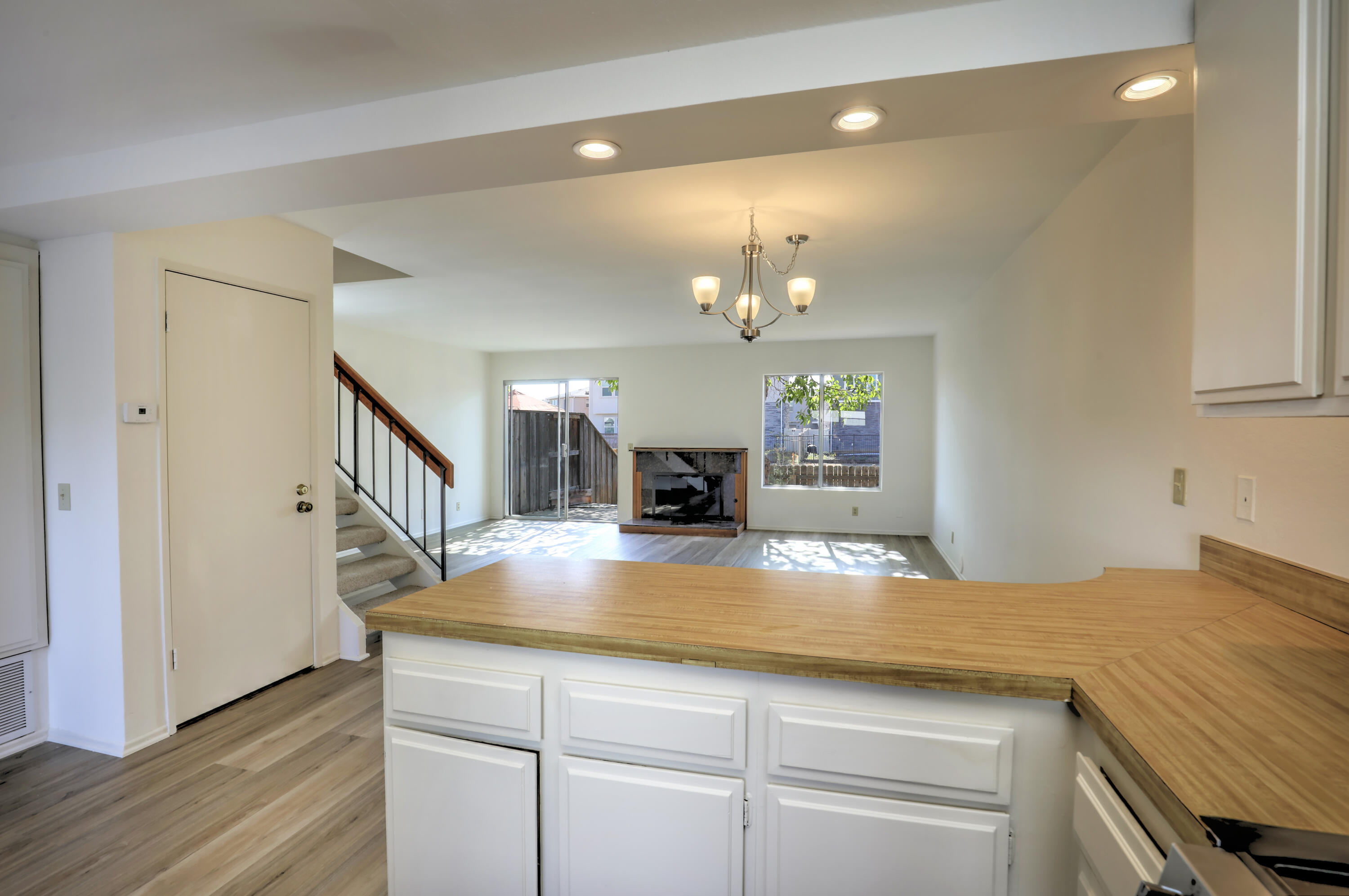 Kitchen with a broad wood countertop overlooking a living room with a fireplace and staircase.
