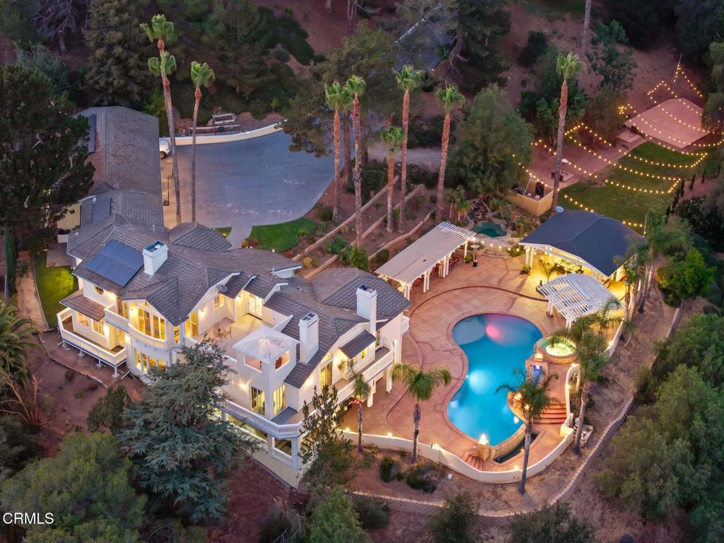 Aerial view of a home with a lit pool, sport court, and event pavilion at dusk.