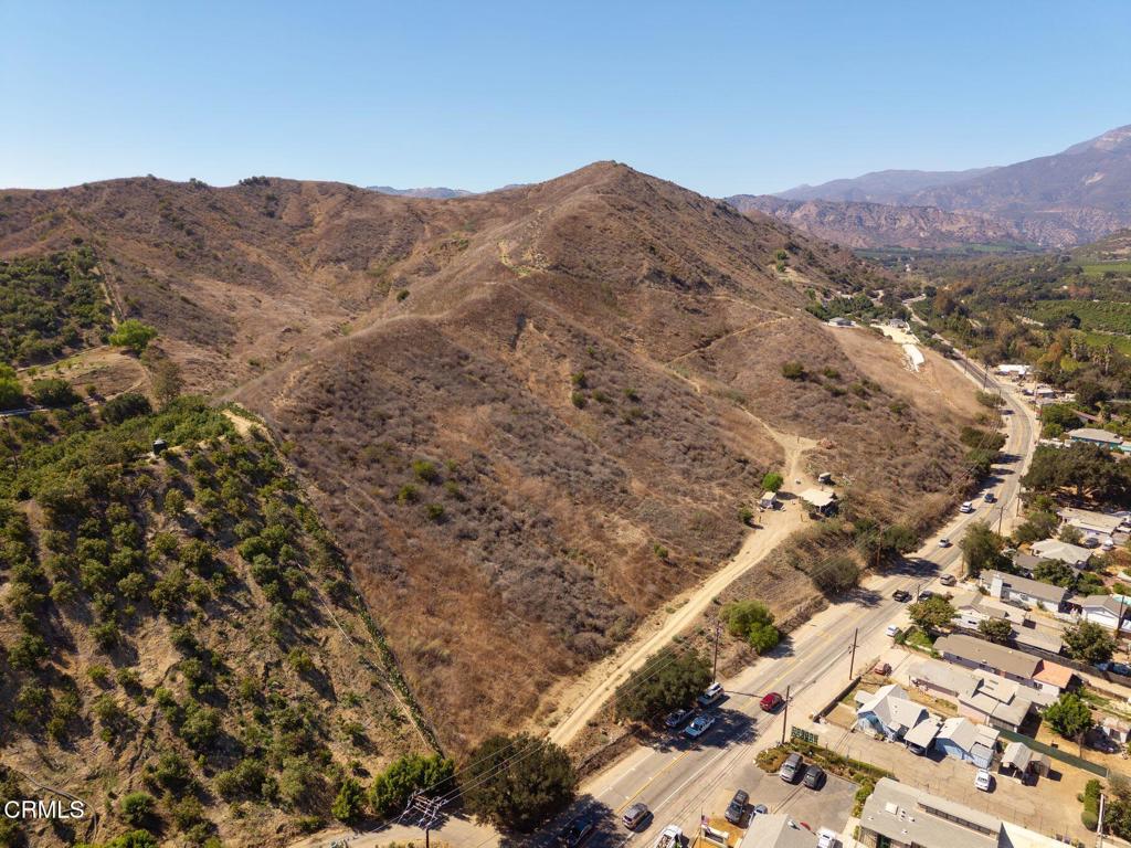 Hilly vacant land beside a paved road, with a dirt track and mountains beyond.