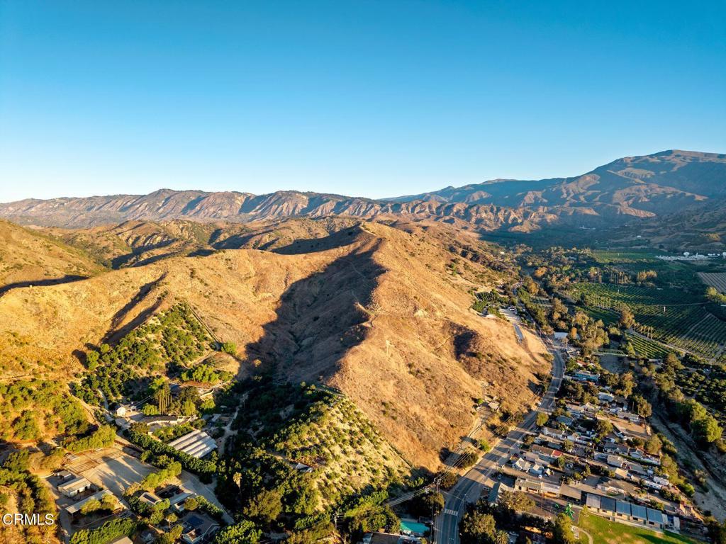 Aerial view of dry hills and open land, with distant mountains, orchards, and homes.