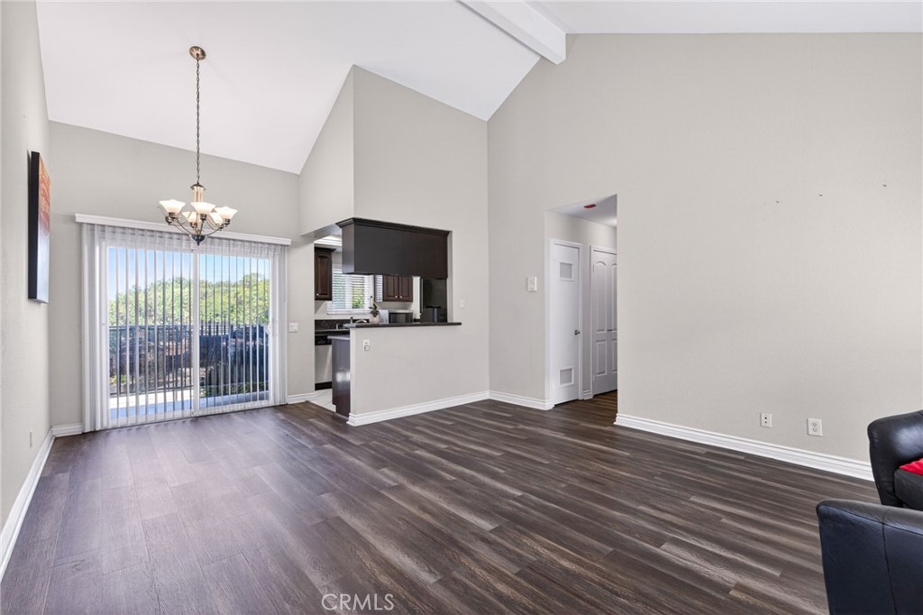 Open living and dining area with dark wood flooring, vaulted ceiling, and sliding glass doors.