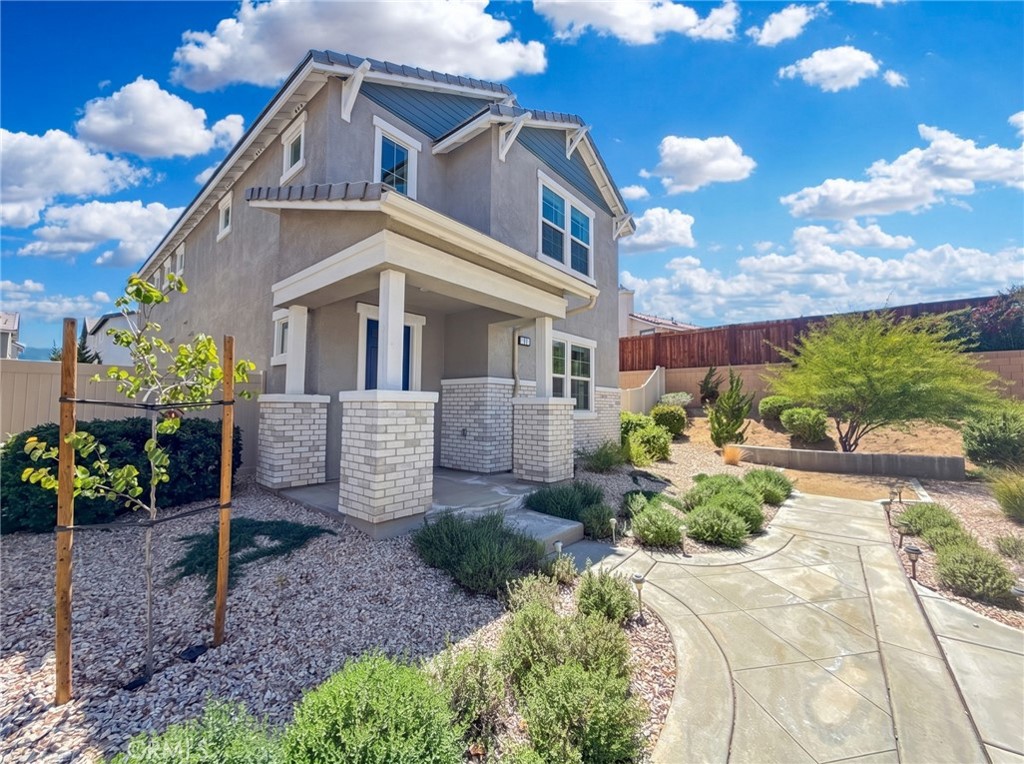 Two-story gray stucco house with a covered porch, brick columns, and drought-tolerant landscaping.