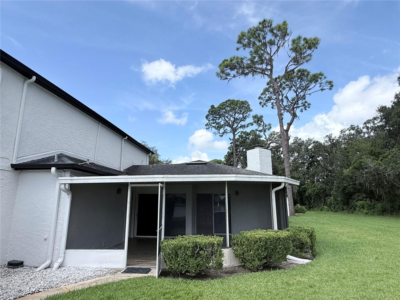 Home’s rear exterior with a screened patio, trimmed shrubs, and a broad green lawn.