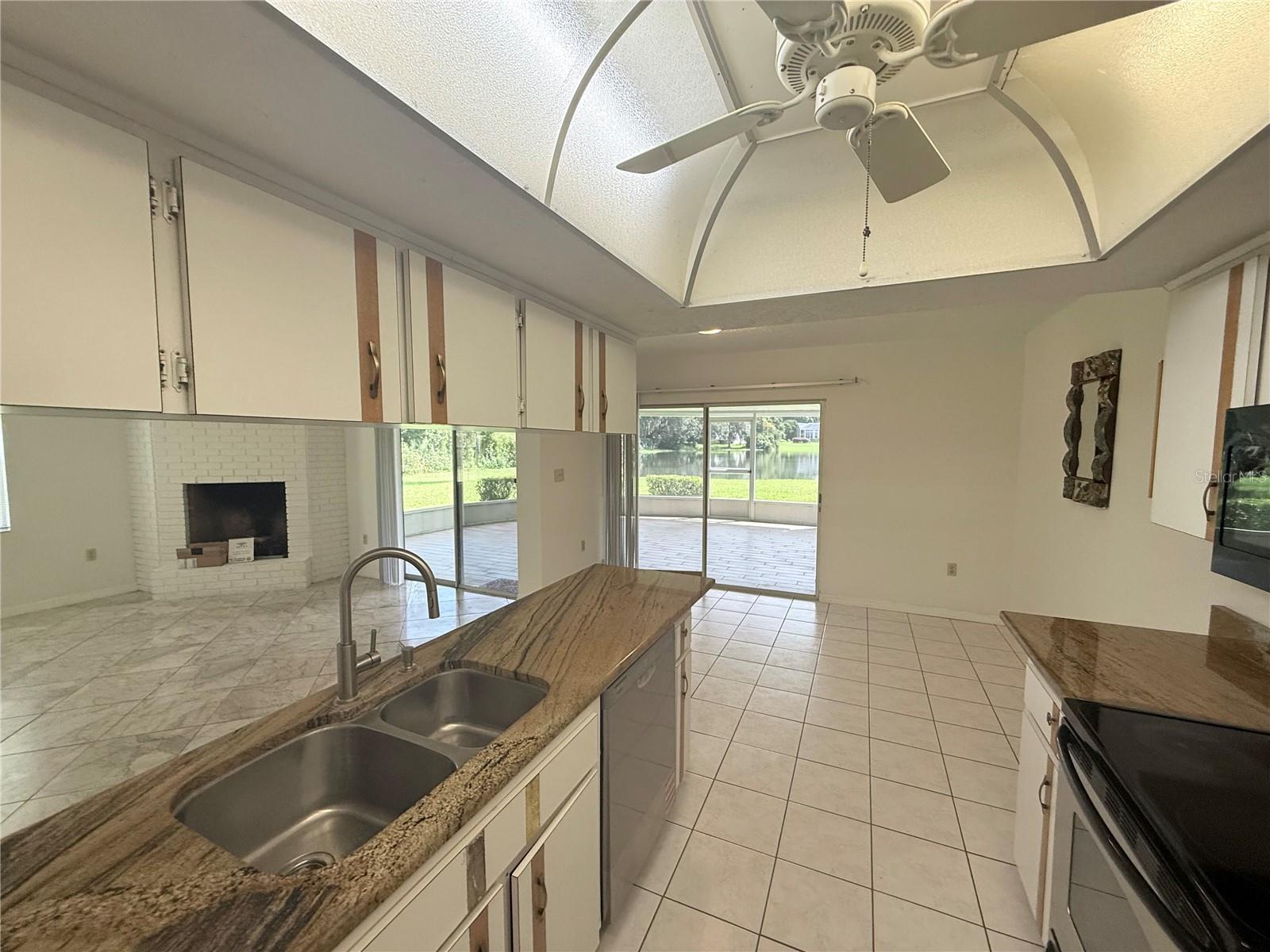 Kitchen with granite counters and double sink, opening to a patio with a pond view.