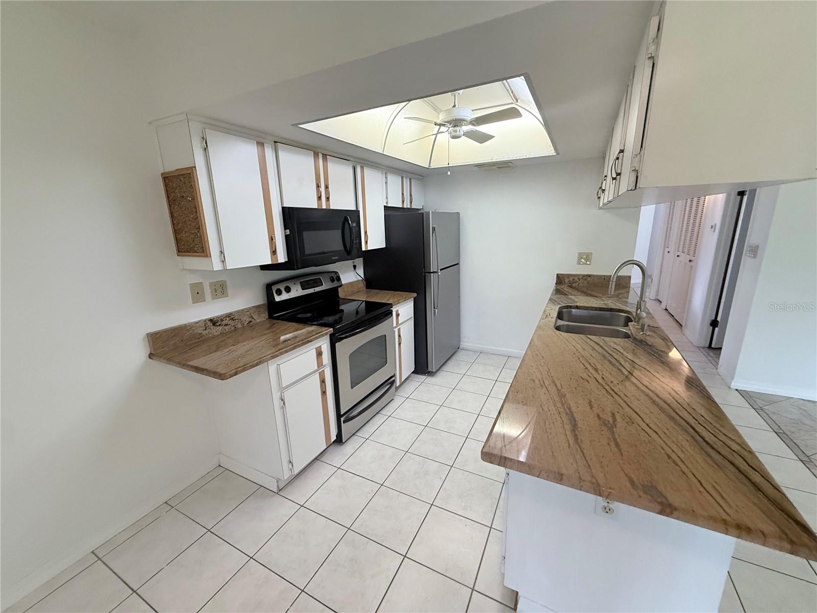Kitchen with a long sink peninsula, tan countertops, and black-and-stainless appliances.