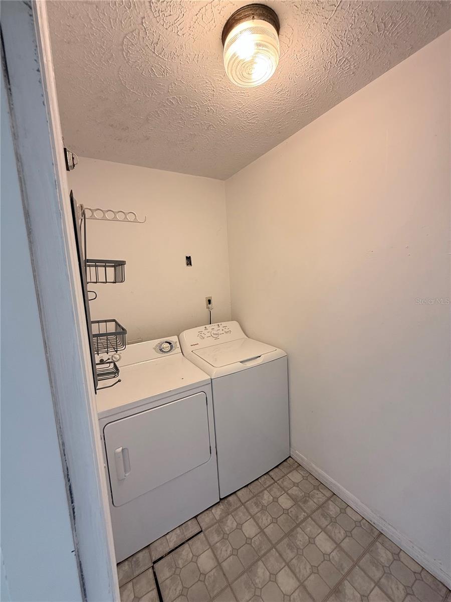 Laundry room with a white washer and dryer, wall-mounted wire racks, and patterned tile flooring.
