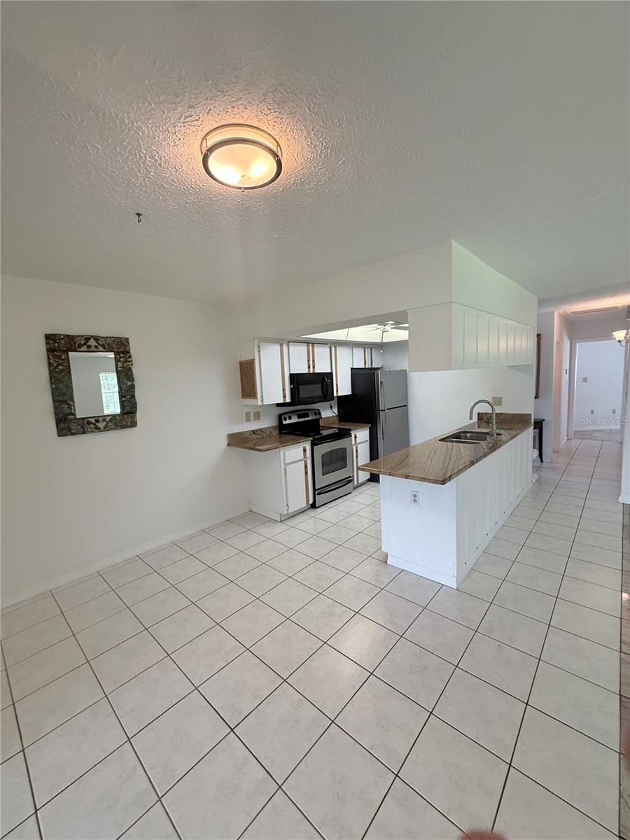 Vacant kitchen with a long island, sink, white cabinets, stainless-steel appliances, and tiled floors.