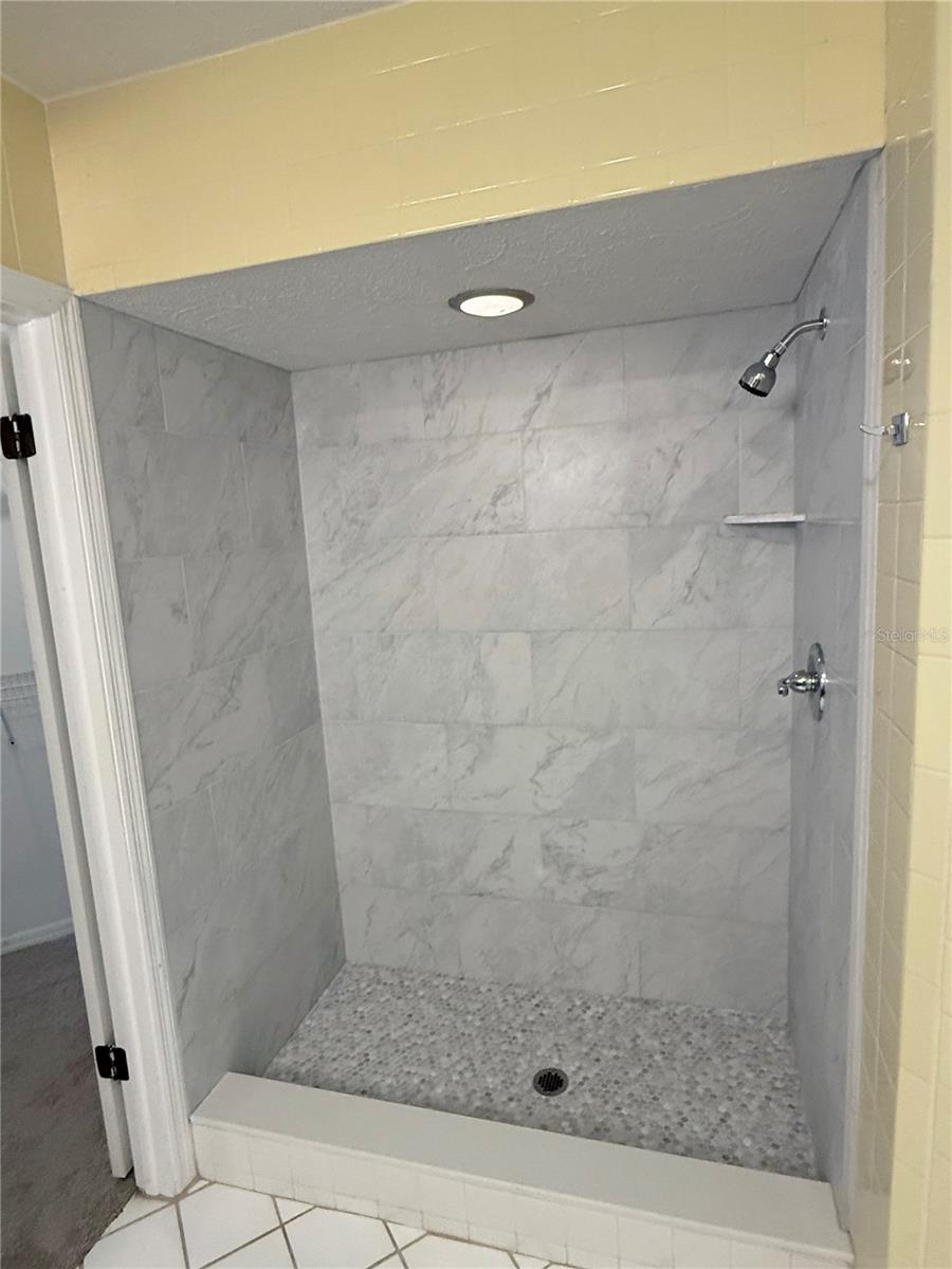 Walk-in shower with gray marble-look tile walls and a small mosaic floor.