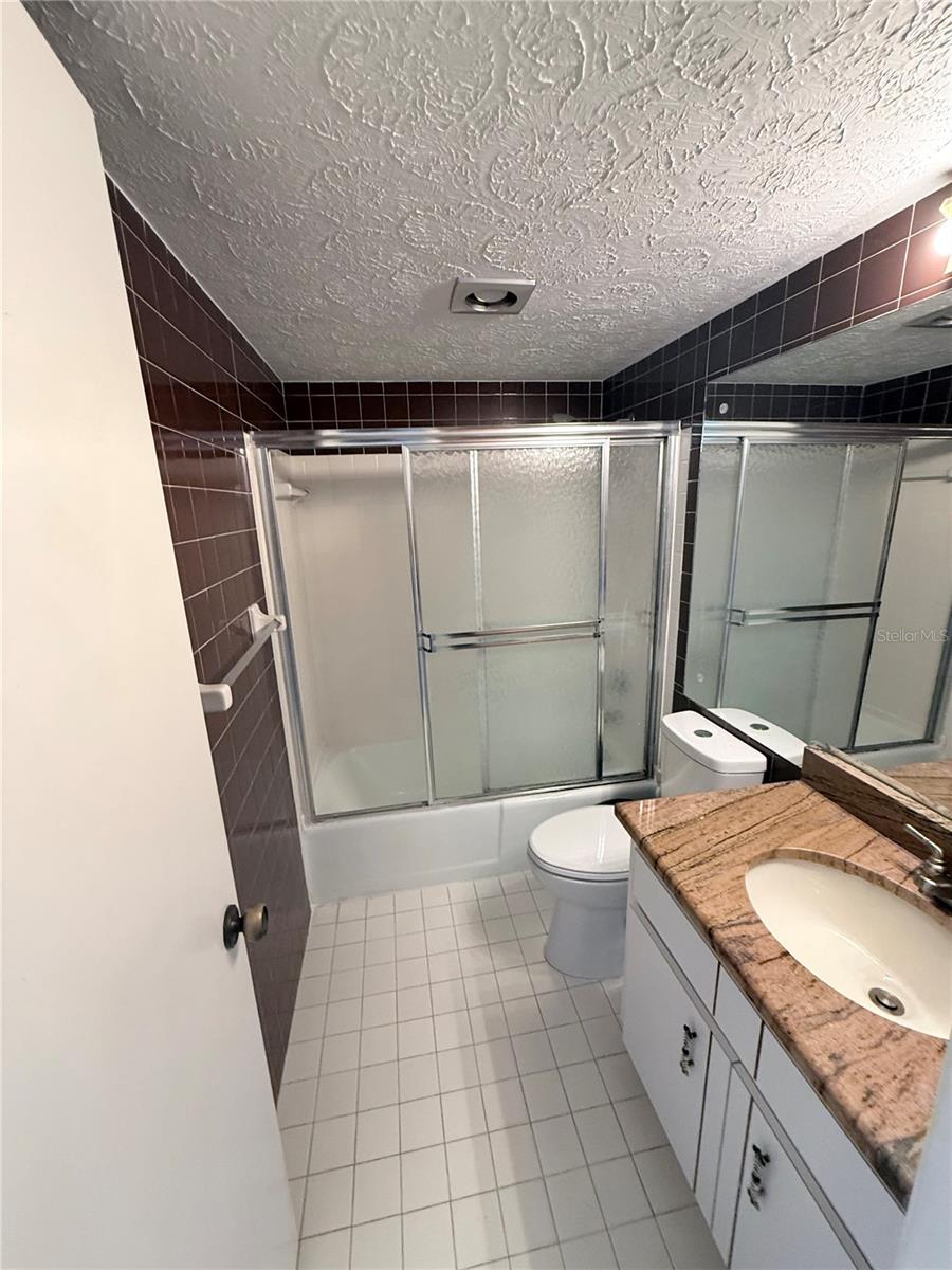Bathroom with a glass-enclosed tub and shower, dark tiled walls, and a stone-topped vanity.