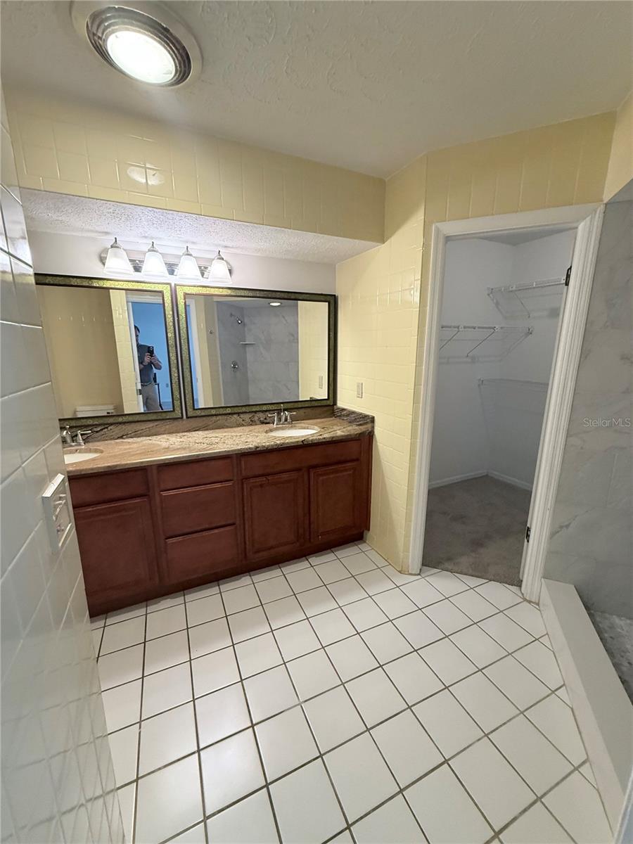 Bathroom with a double vanity, two mirrors, tiled floor, and an open closet doorway.