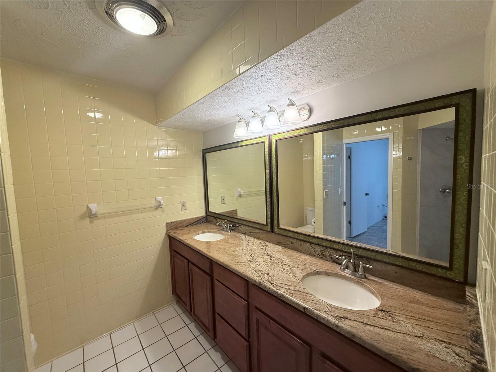 Bathroom with a double-sink granite vanity, dark wood cabinets, and large mirrors.