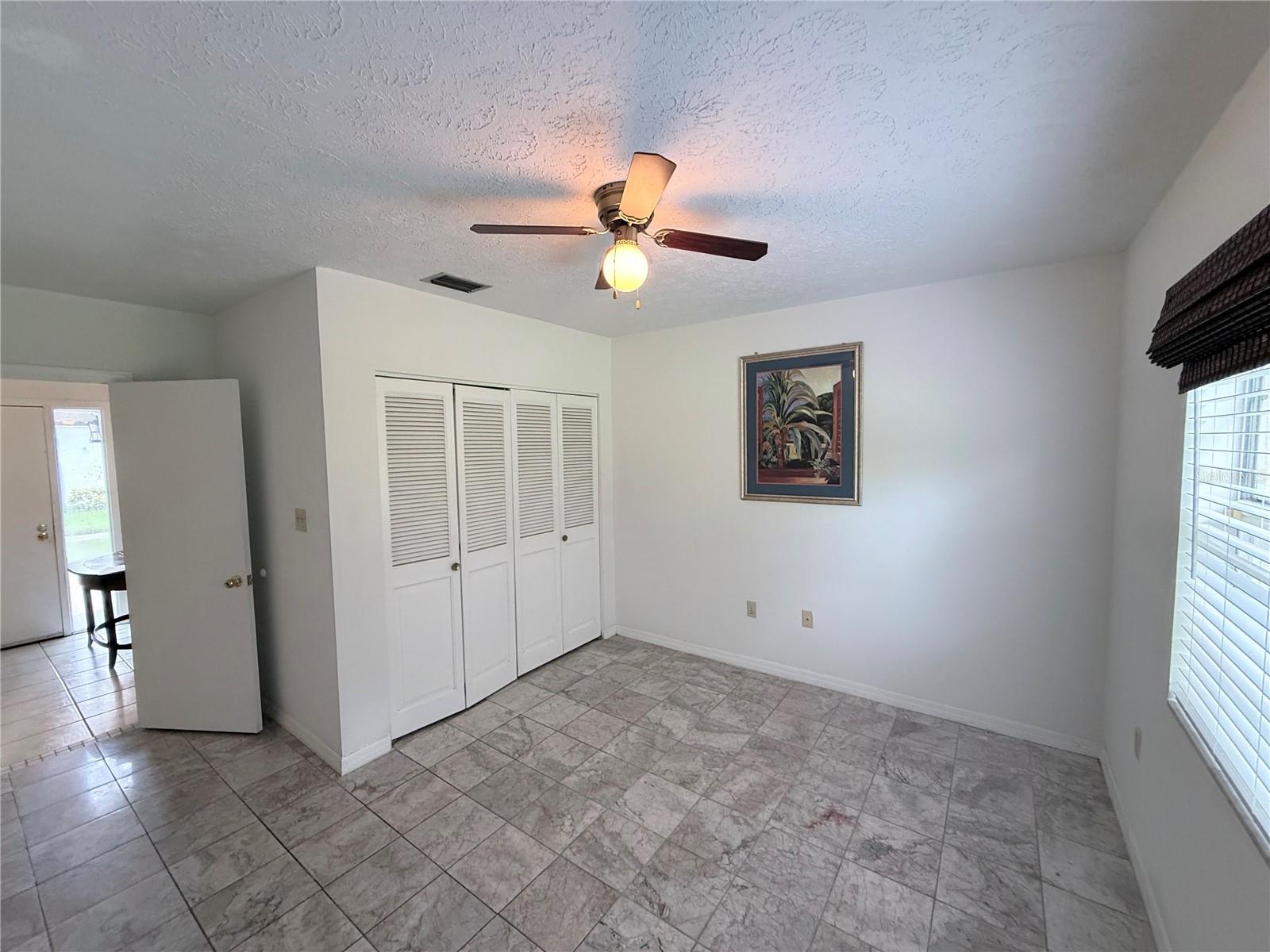 Empty bedroom with tiled floors, a louvered closet, and a ceiling fan.
