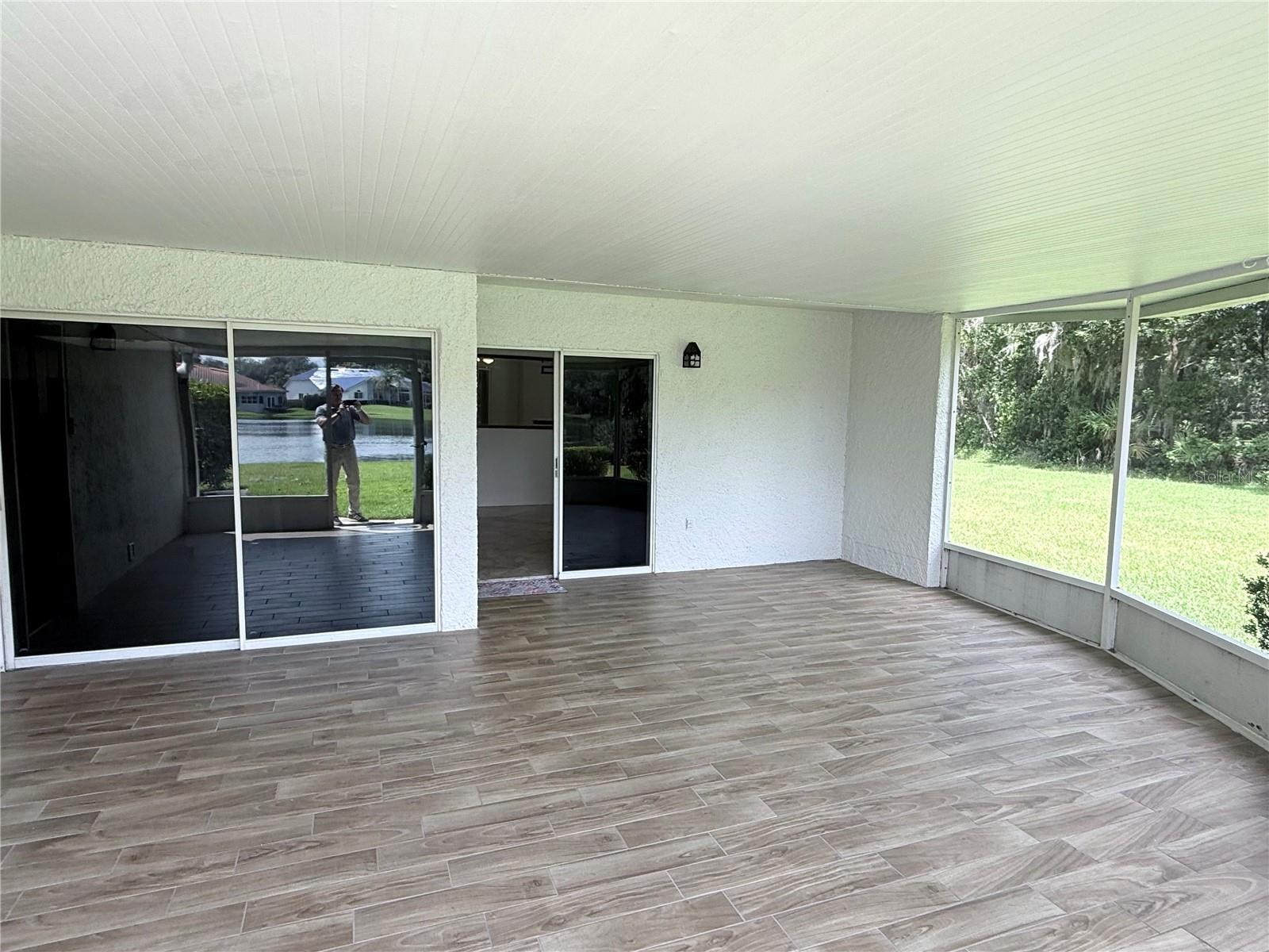 Screened patio with wood-look tile flooring and sliding doors overlooking a pond.